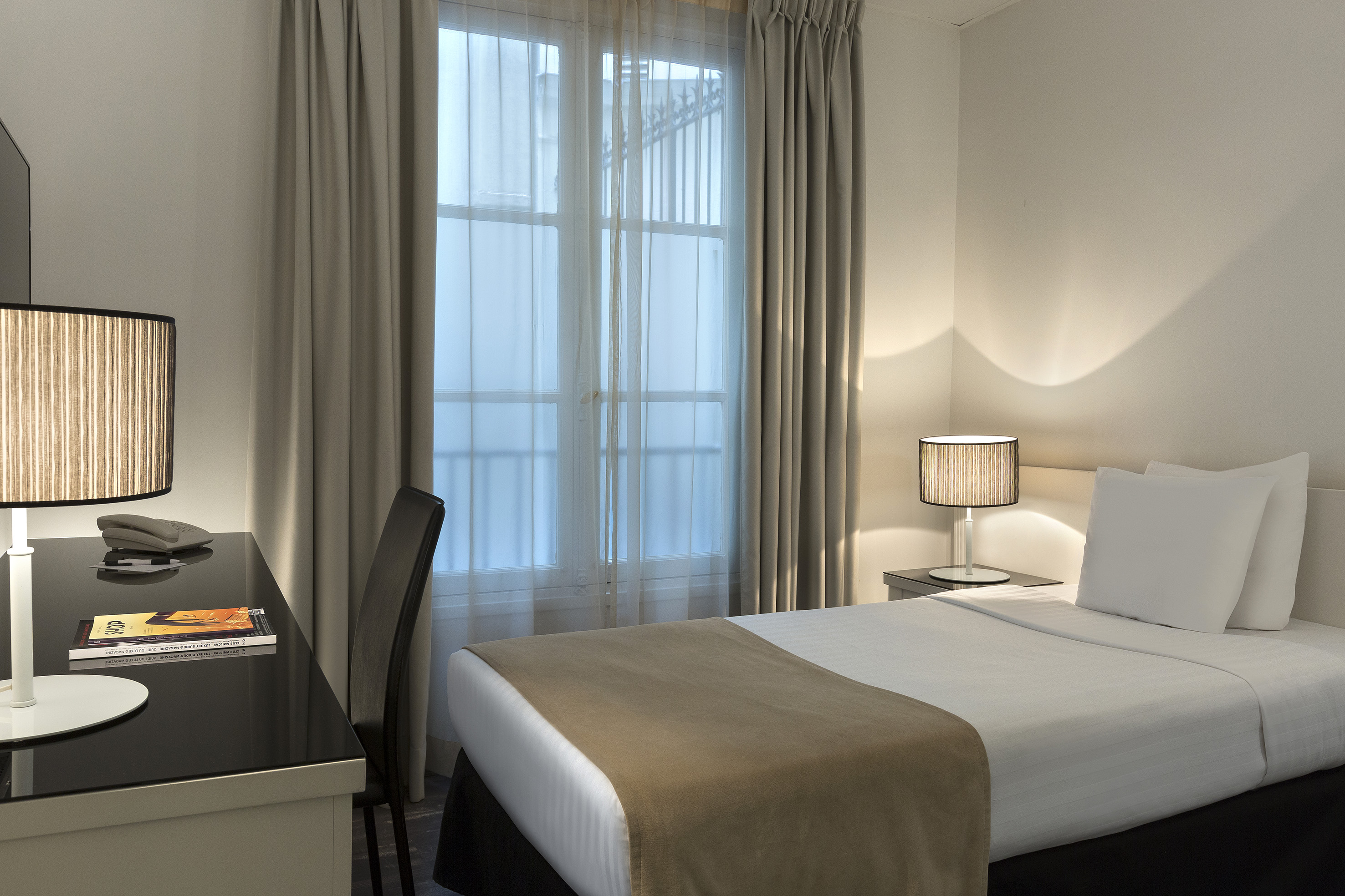 Hotel guest room with single bed, desk, lamp, and window.