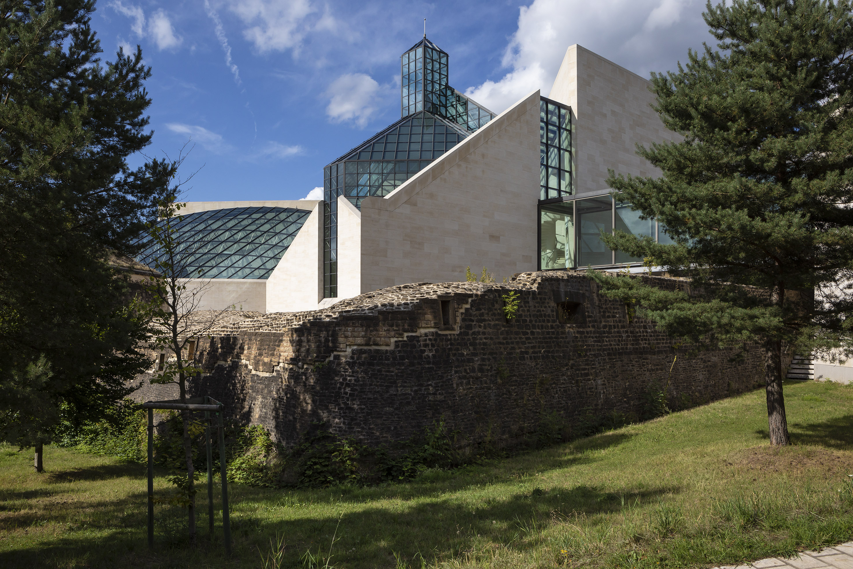 Modern glass and stone building contrasting with ancient stone wall.