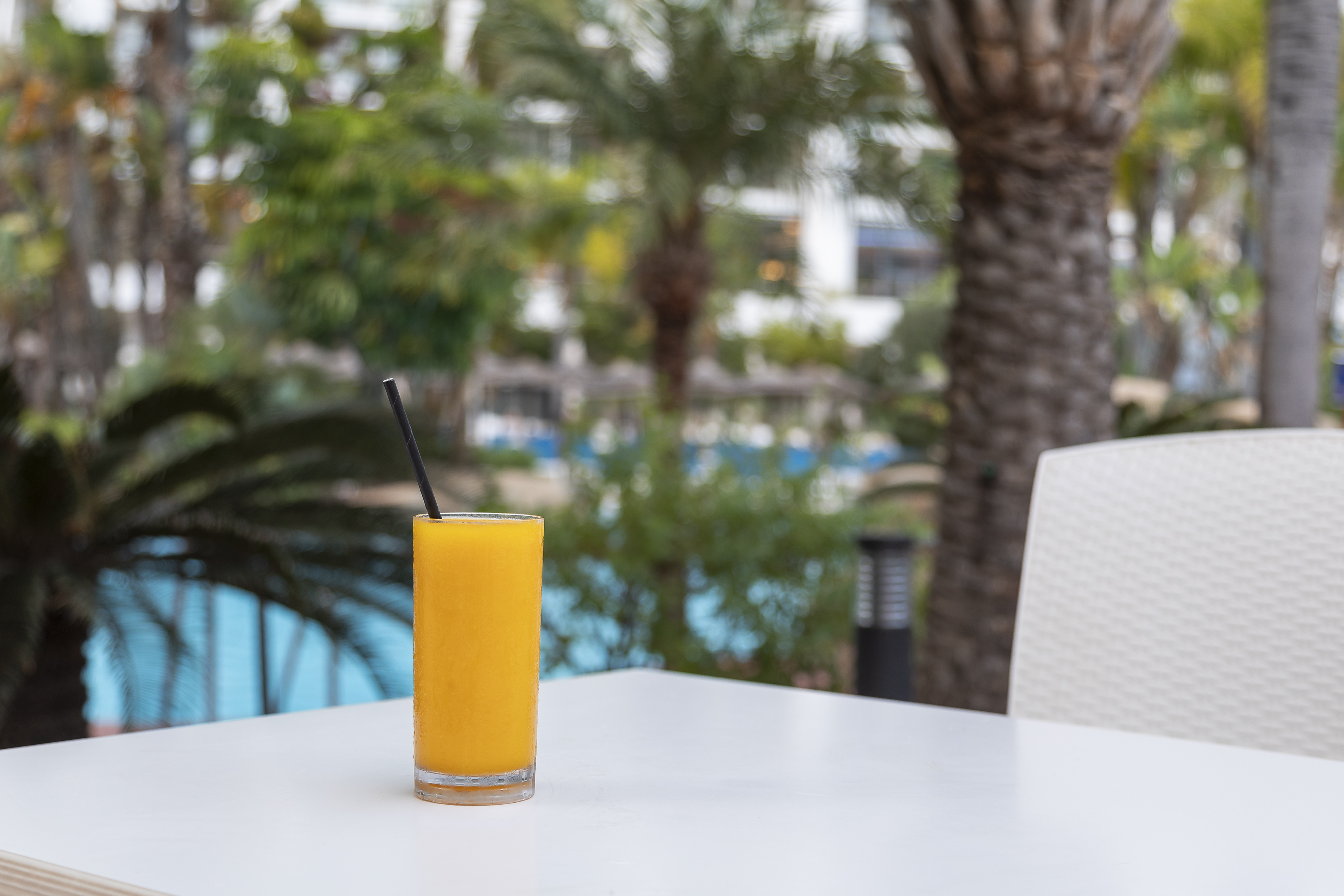 Refreshing tropical orange juice with straw on white table, poolside.