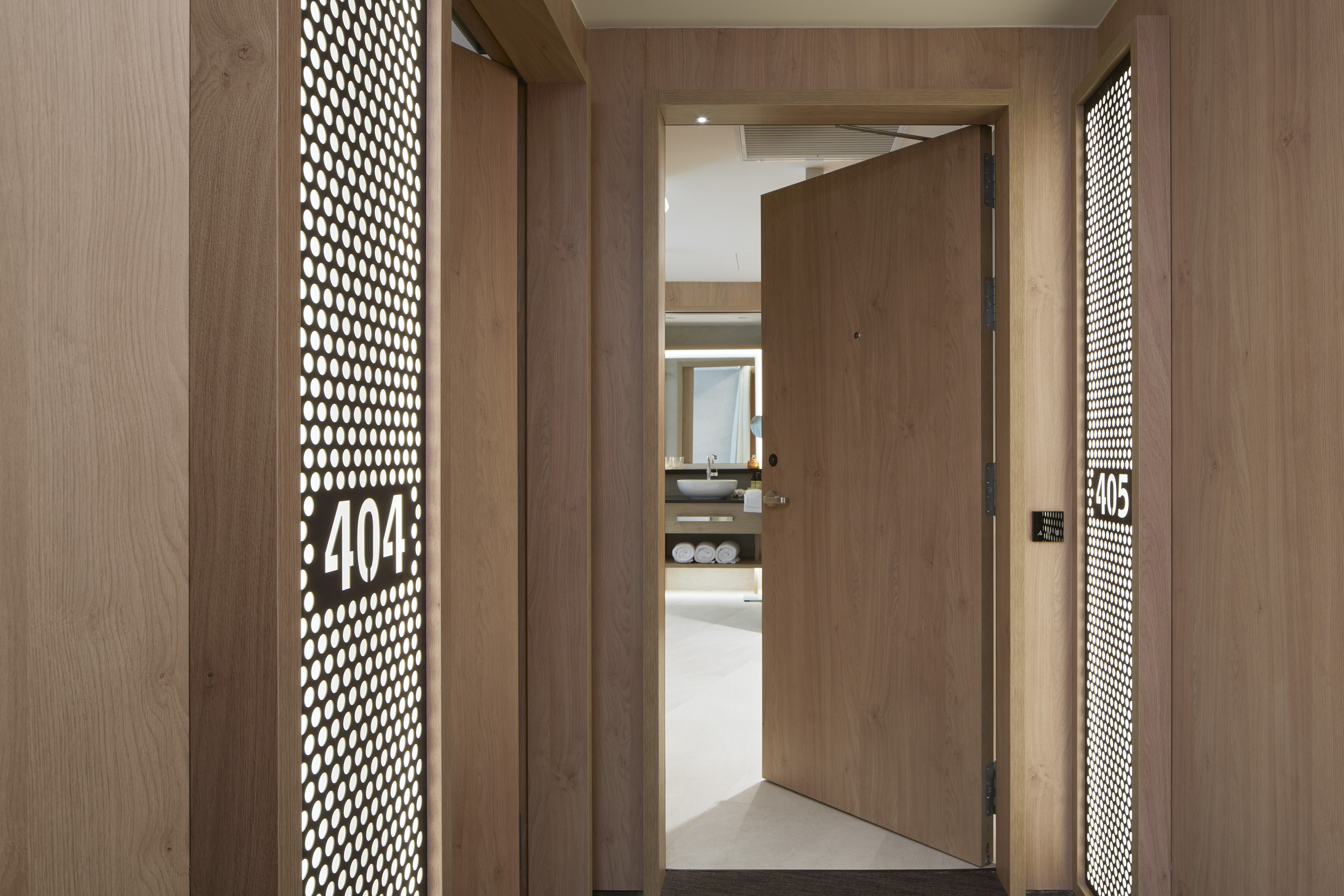 Modern hotel hallway, wood paneling, illuminated room numbers 404, 405, open bathroom.