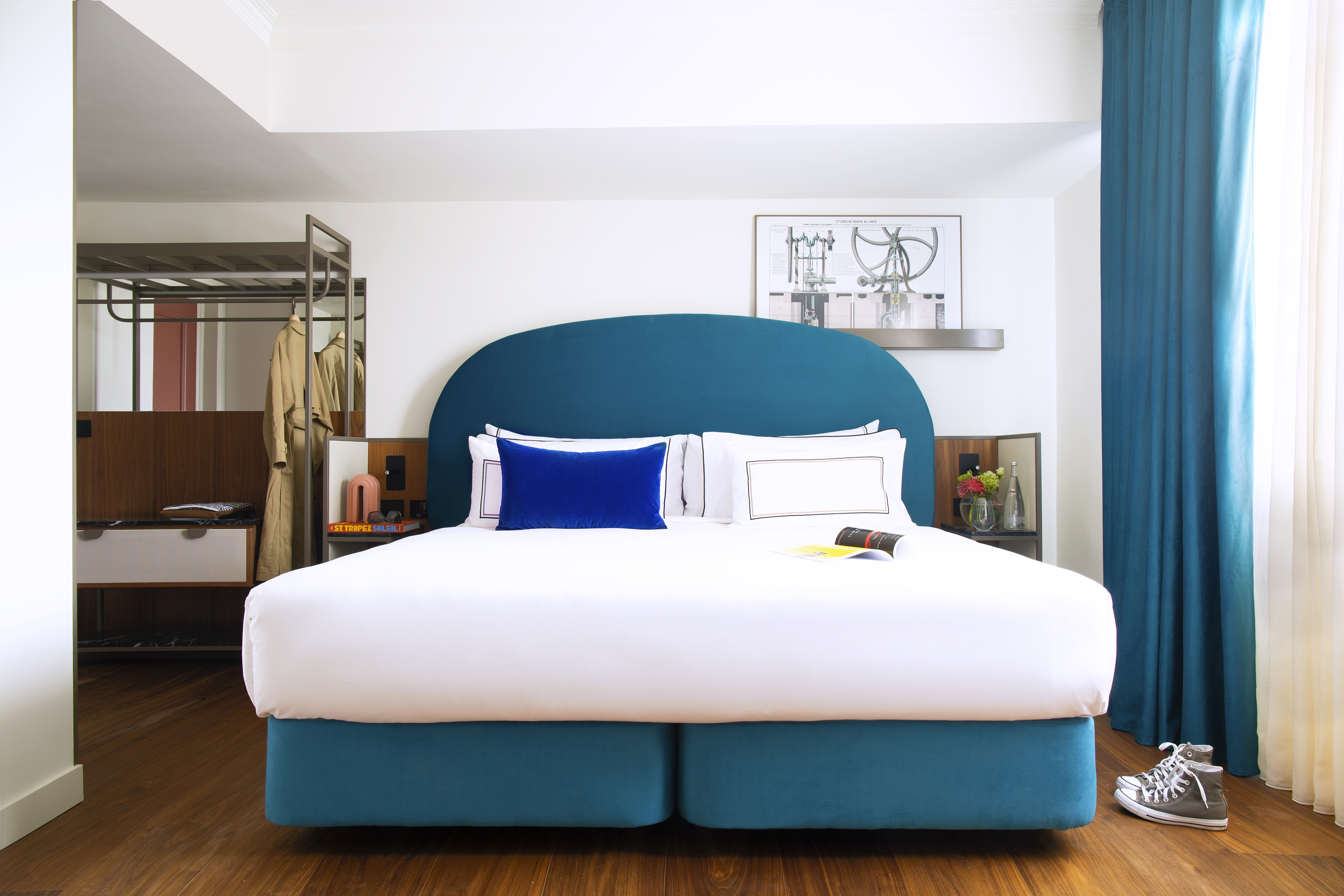 Contemporary hotel room with blue bed, white linens, and hardwood floor.