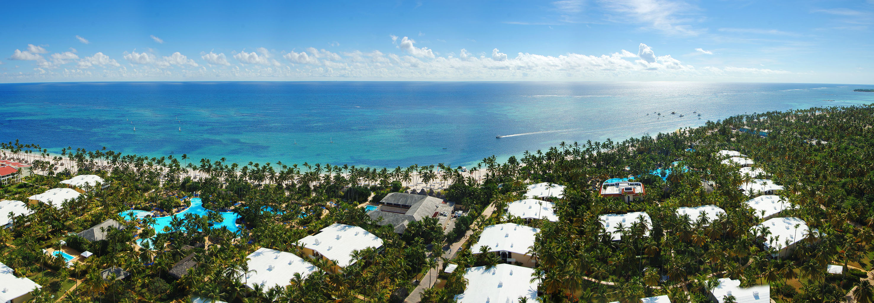 Tropical beach resort aerial: blue ocean, white sand, palm trees, and pools.