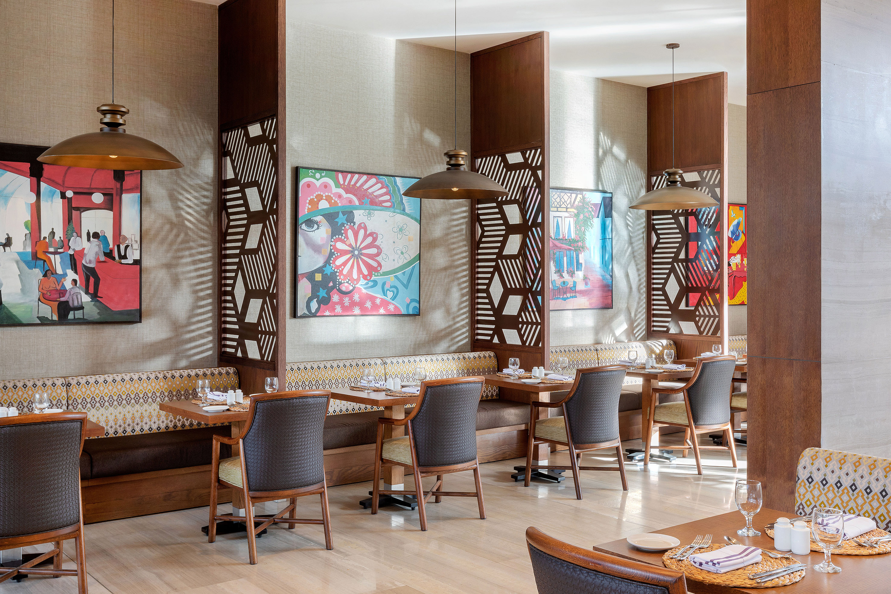 Restaurant dining area with colorful art, patterned booth seating, and pendant lights.