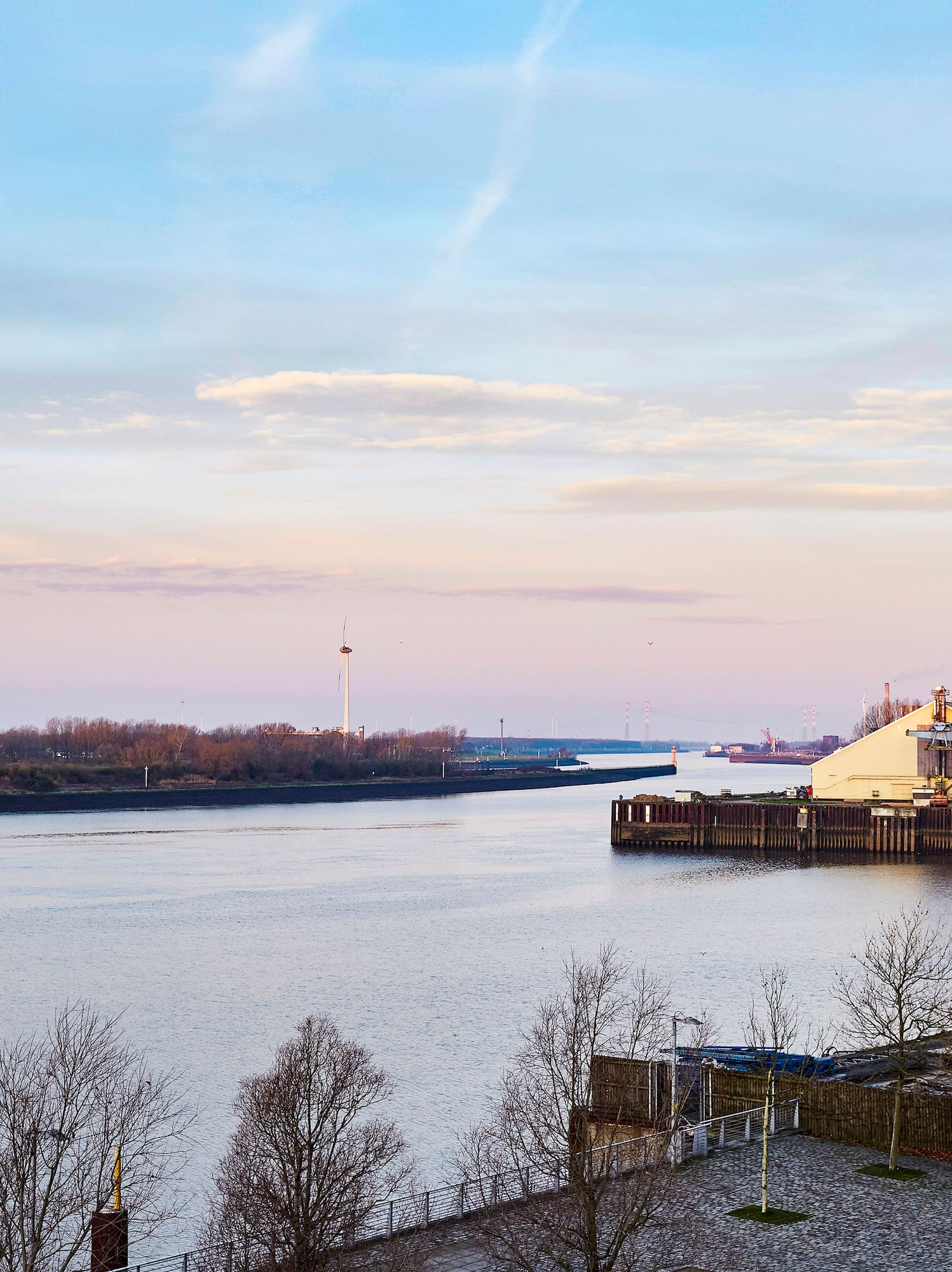 Industrial river port with silos, docks, and winter trees at twilight.
