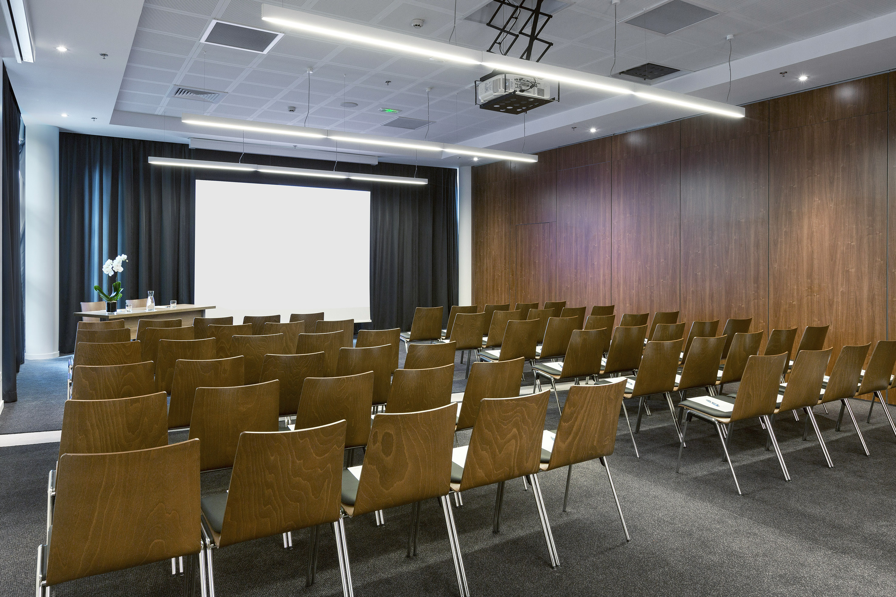 Empty modern conference room with wooden chairs, projector, and screen.