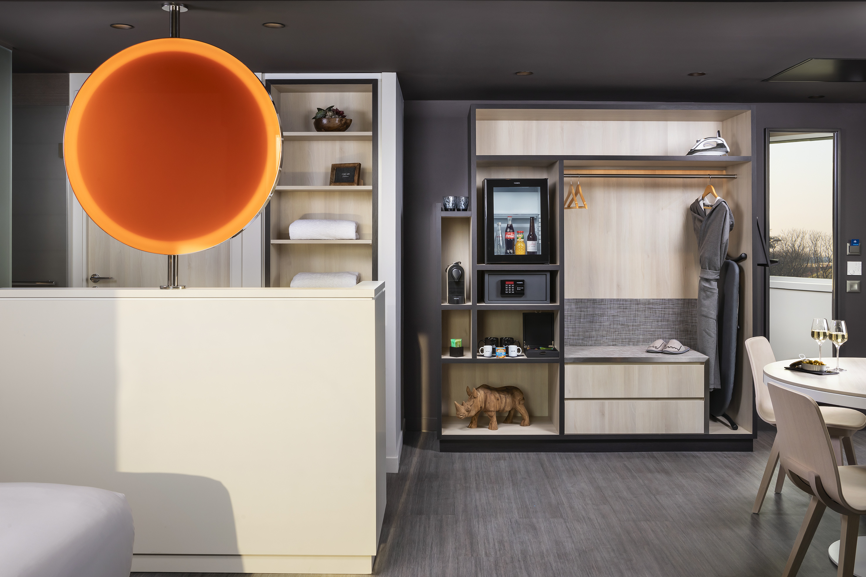 Stylish hotel room with orange lamp, open wardrobe, mini-bar, and amenities.