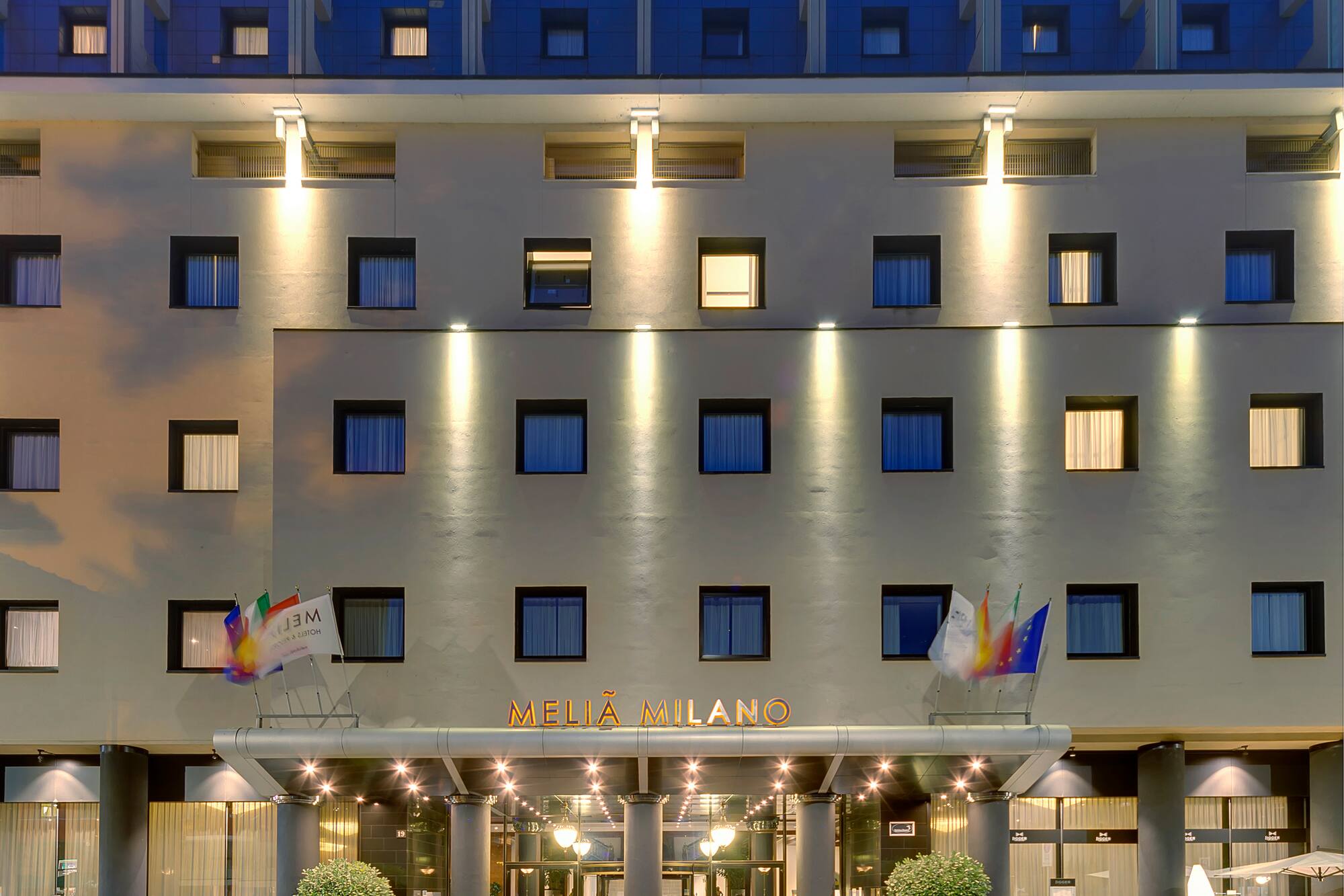Melia Milano hotel exterior at night with illuminated entrance and windows.