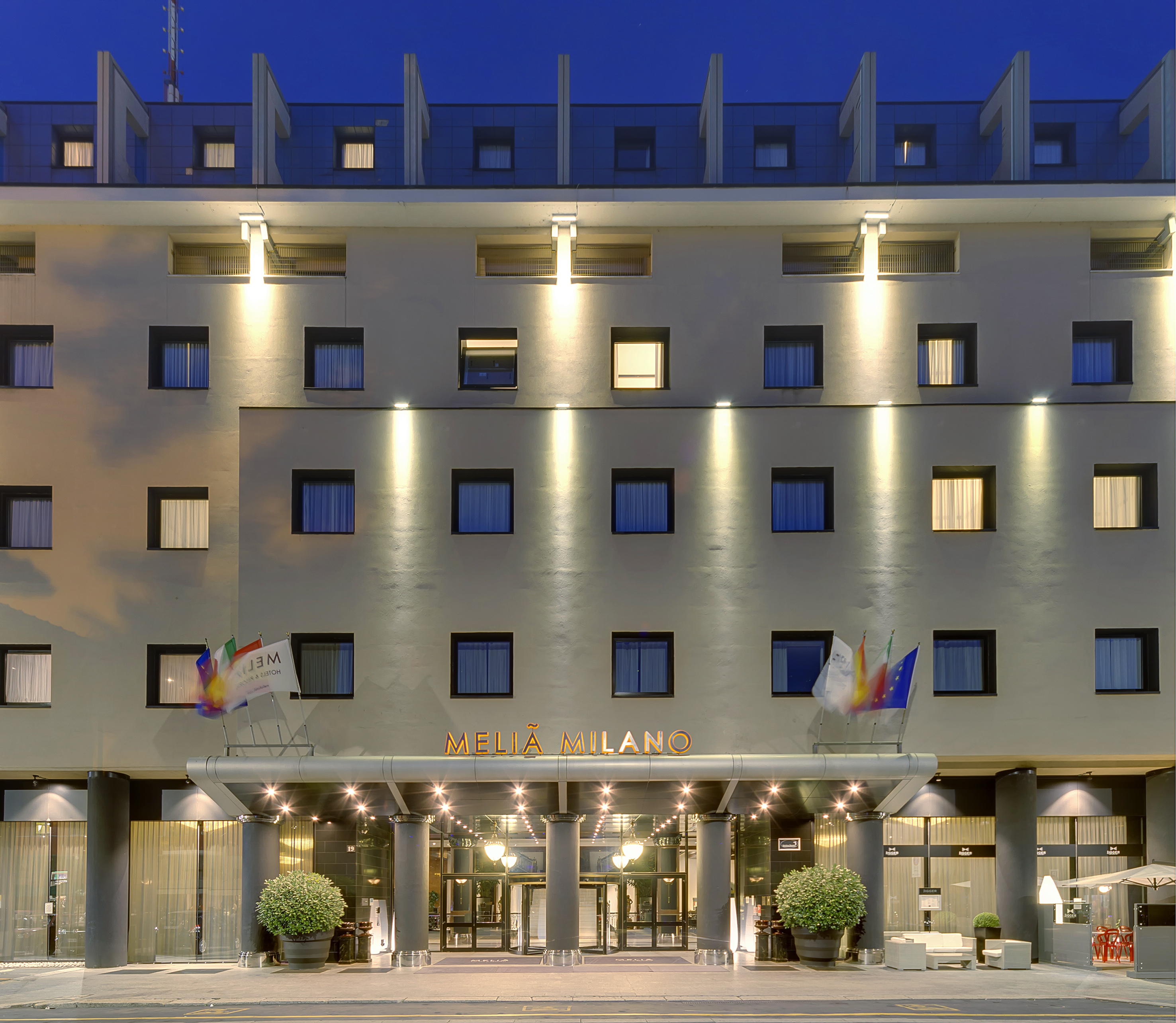 Melia Milano hotel exterior at night with illuminated entrance and windows.