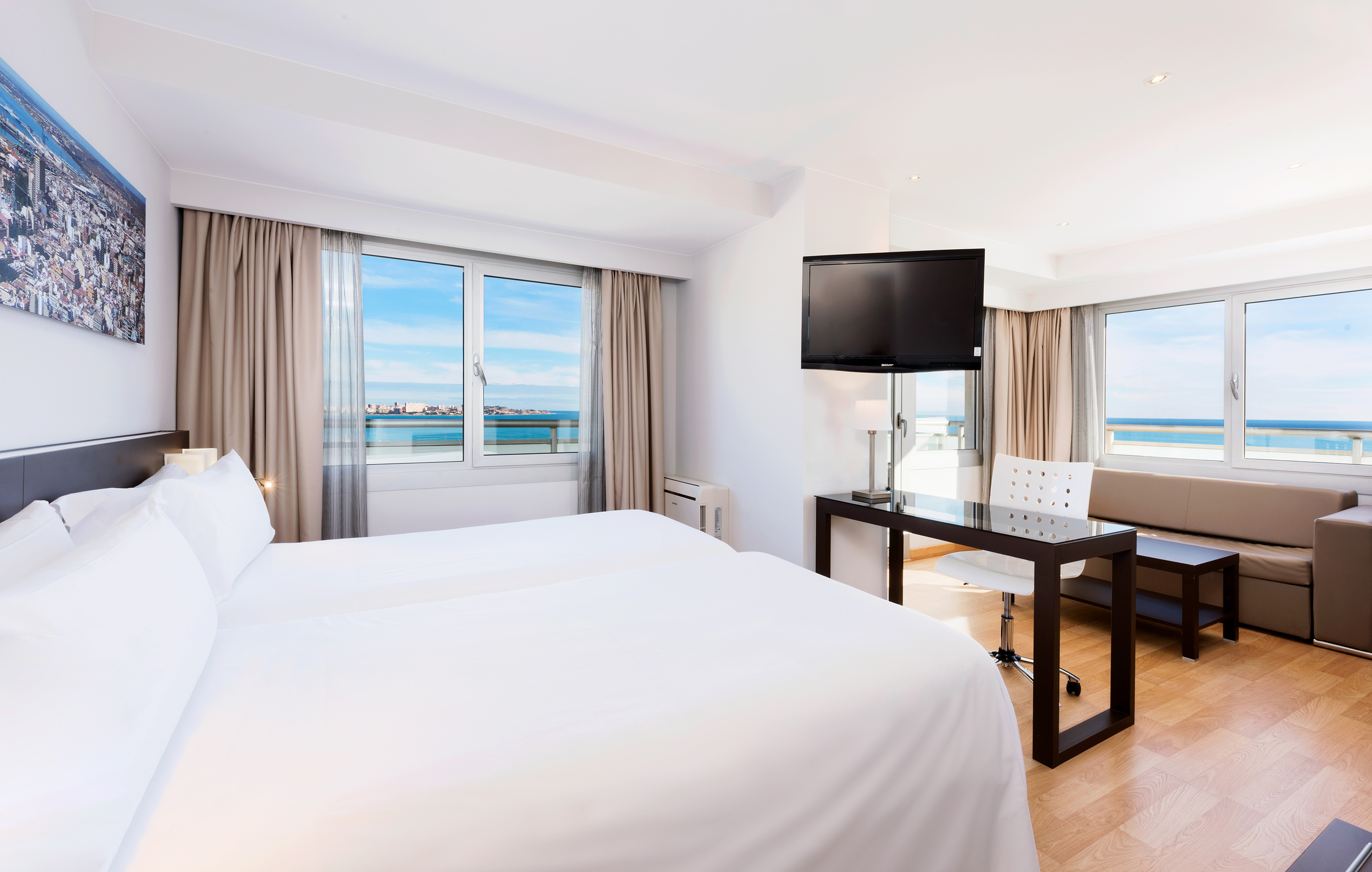 Modern hotel room with twin beds, desk, and expansive sea view.