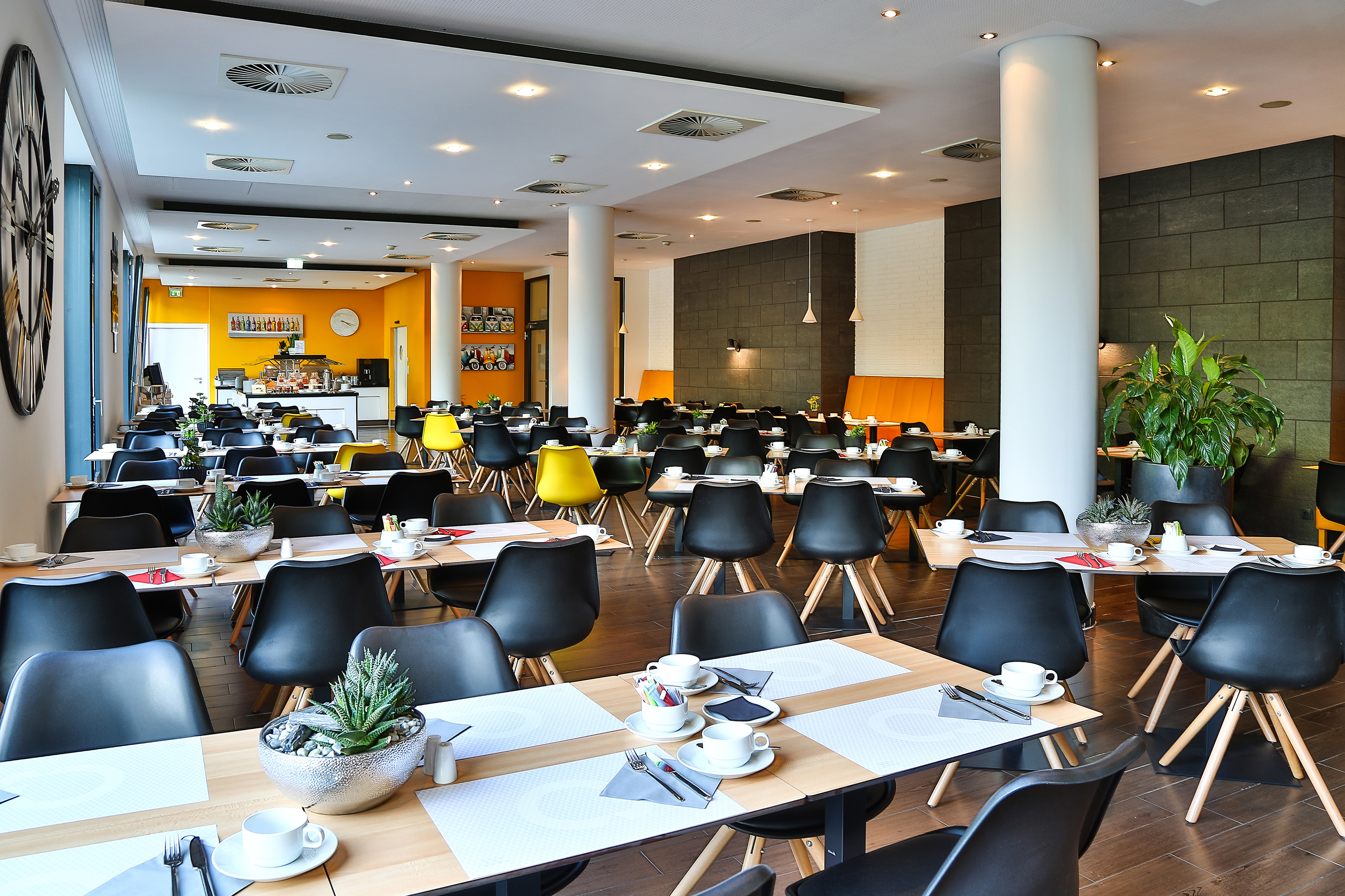 Modern hotel dining room with black chairs, set tables, and breakfast buffet.