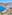 White buildings on a hillside overlooking a bright blue ocean and dark beach.