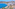White buildings on a hillside overlooking a bright blue ocean and dark beach.