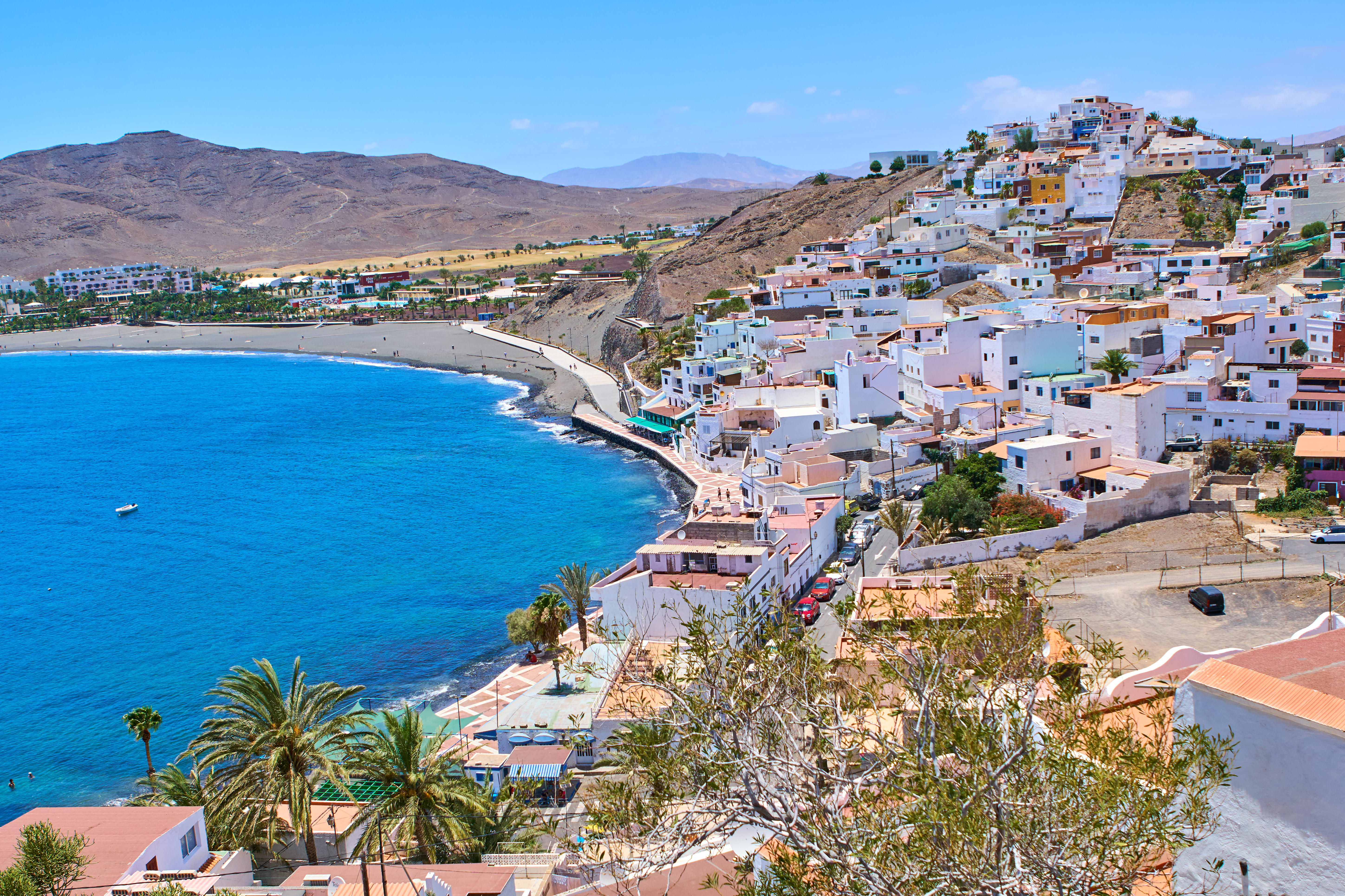 White buildings on a hillside overlooking a bright blue ocean and dark beach.