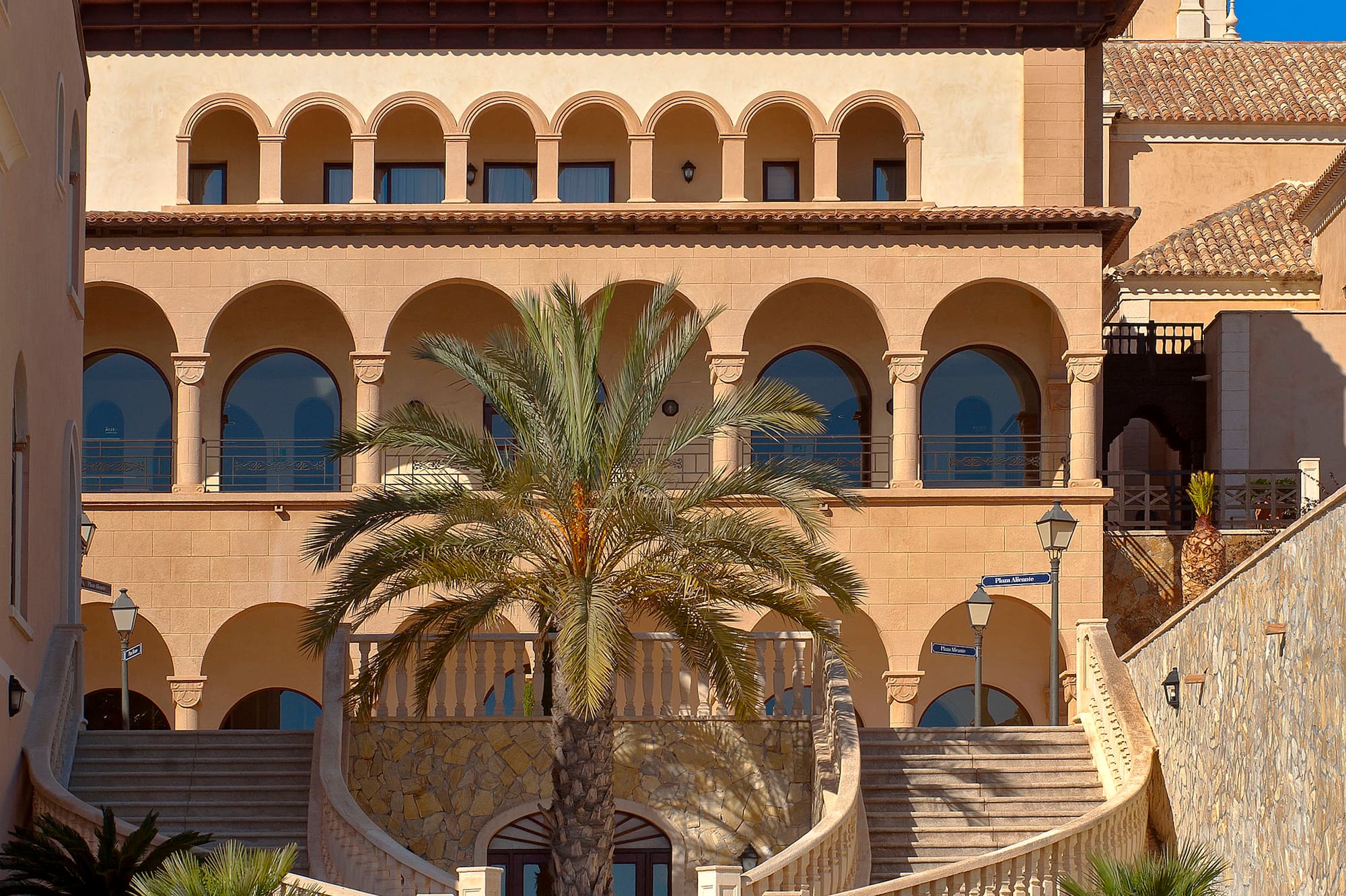 Mediterranean building with arches, clock tower, grand staircase, and palm trees.