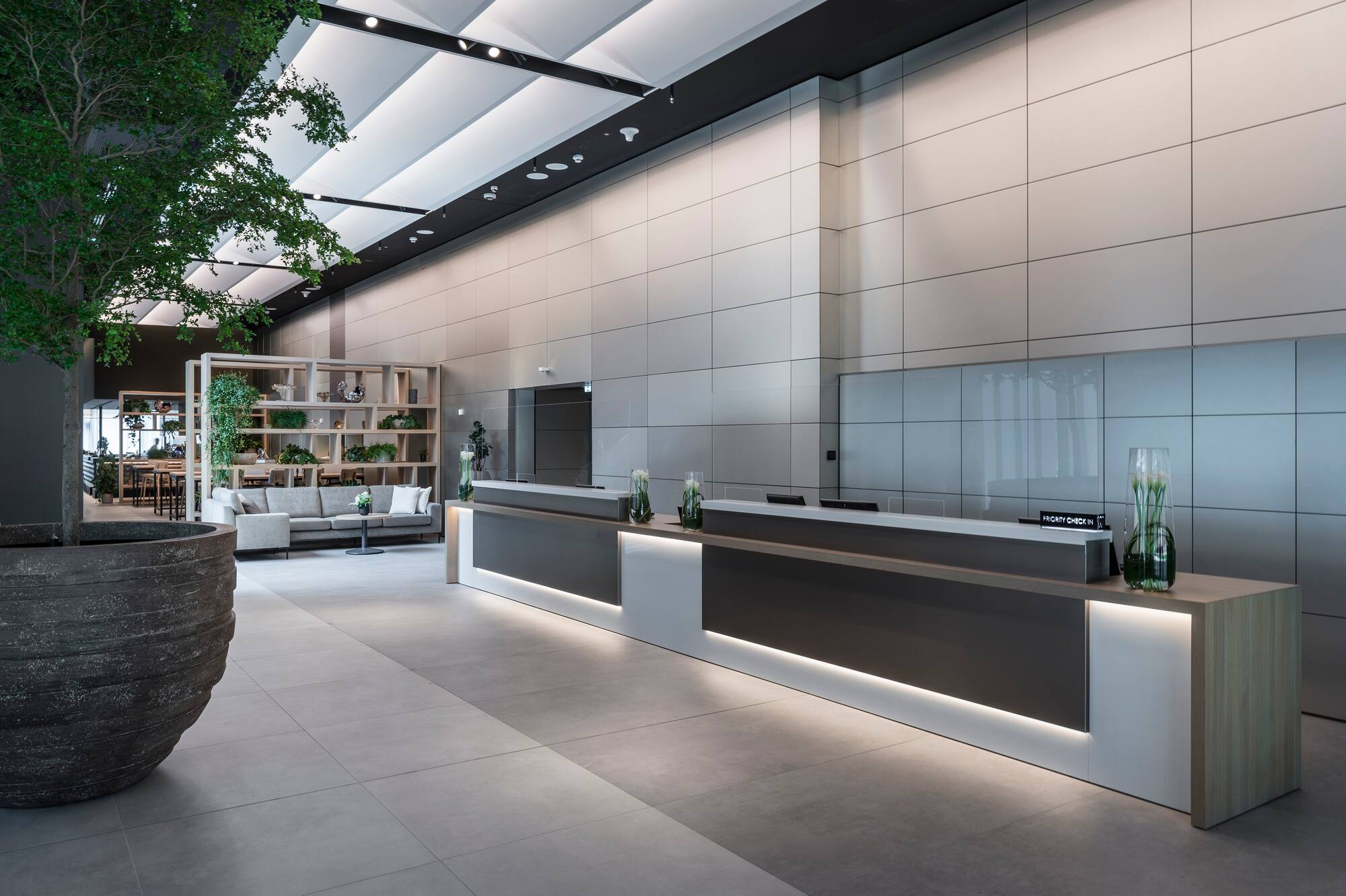 Modern hotel lobby with two backlit reception desks, large tree, and lounge area.
