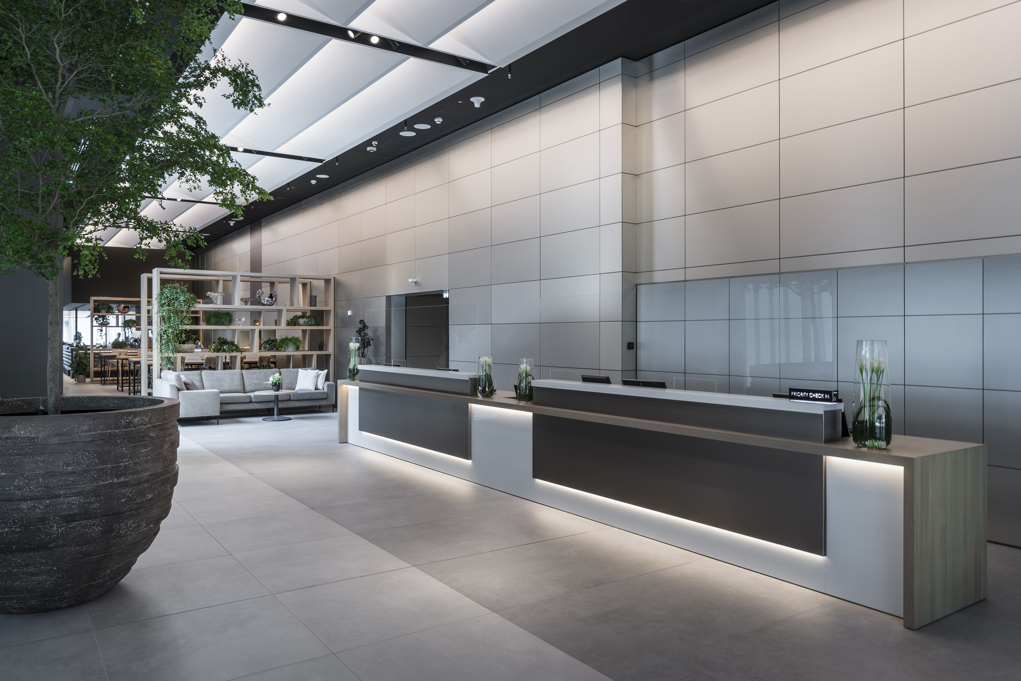 Modern hotel lobby with two backlit reception desks, large tree, and lounge area.