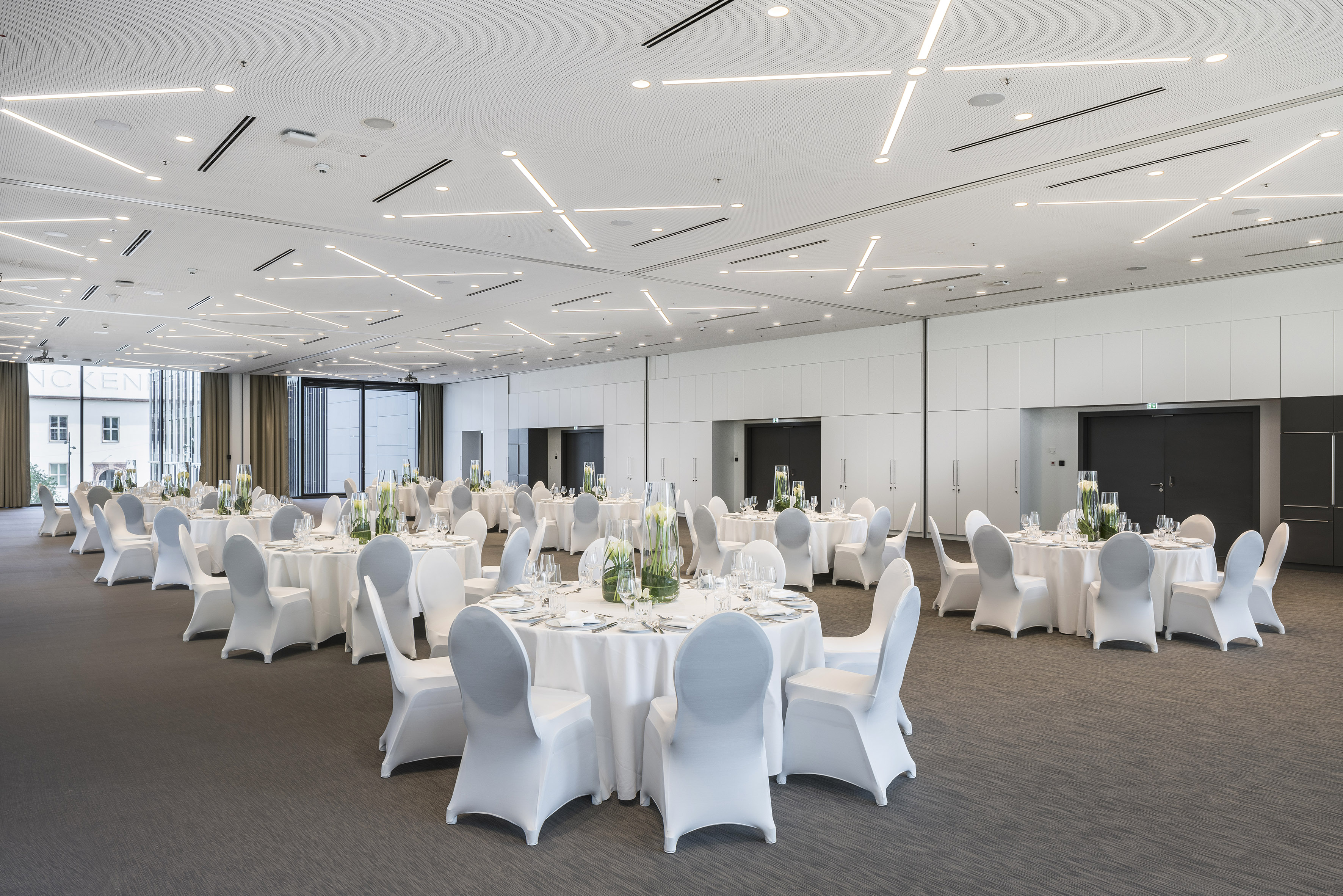 Elegant banquet hall with white tables, chair covers, and modern lighting.
