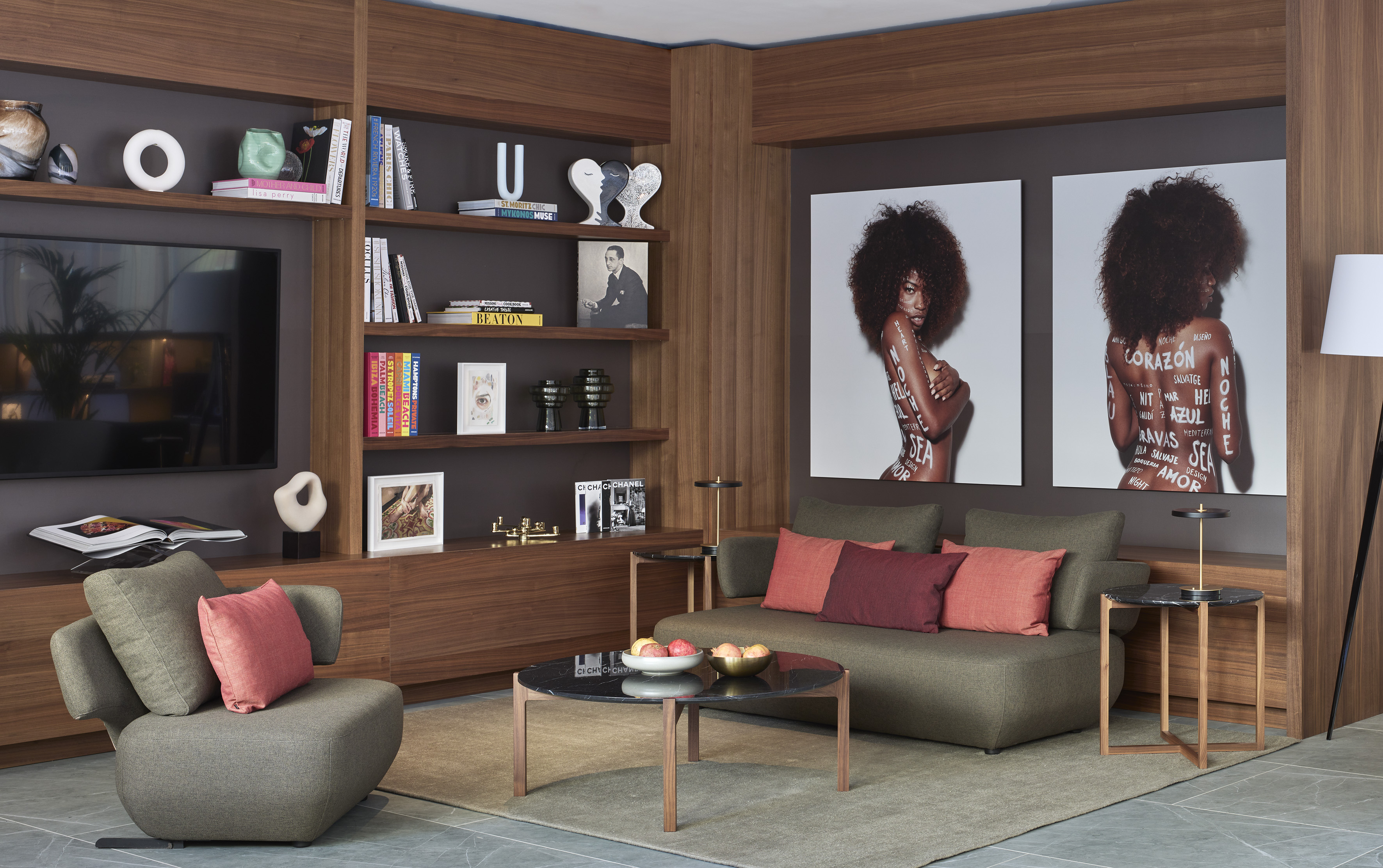 Modern lounge with wood shelves, colorful books, large art prints, green sofa.