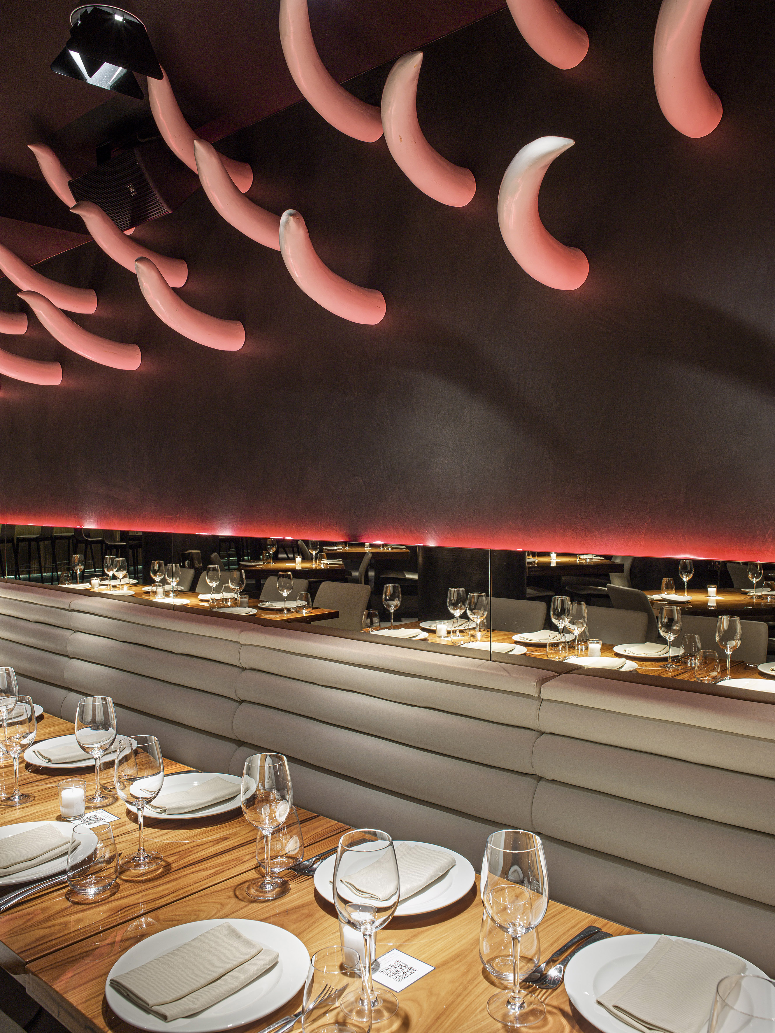 Restaurant dining room with wooden tables, cream booths, curved pink ceiling lights.