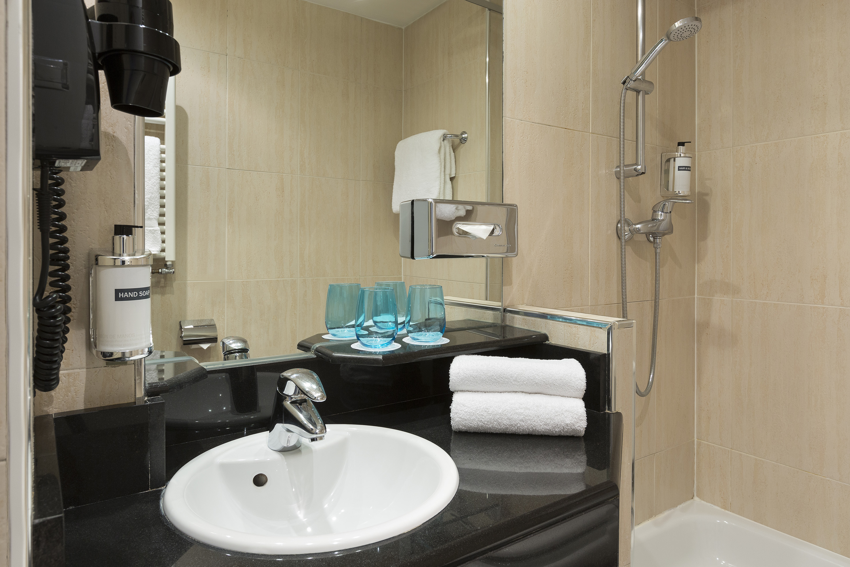 Hotel guest bathroom with vanity, white sink, shower, and fresh towels.