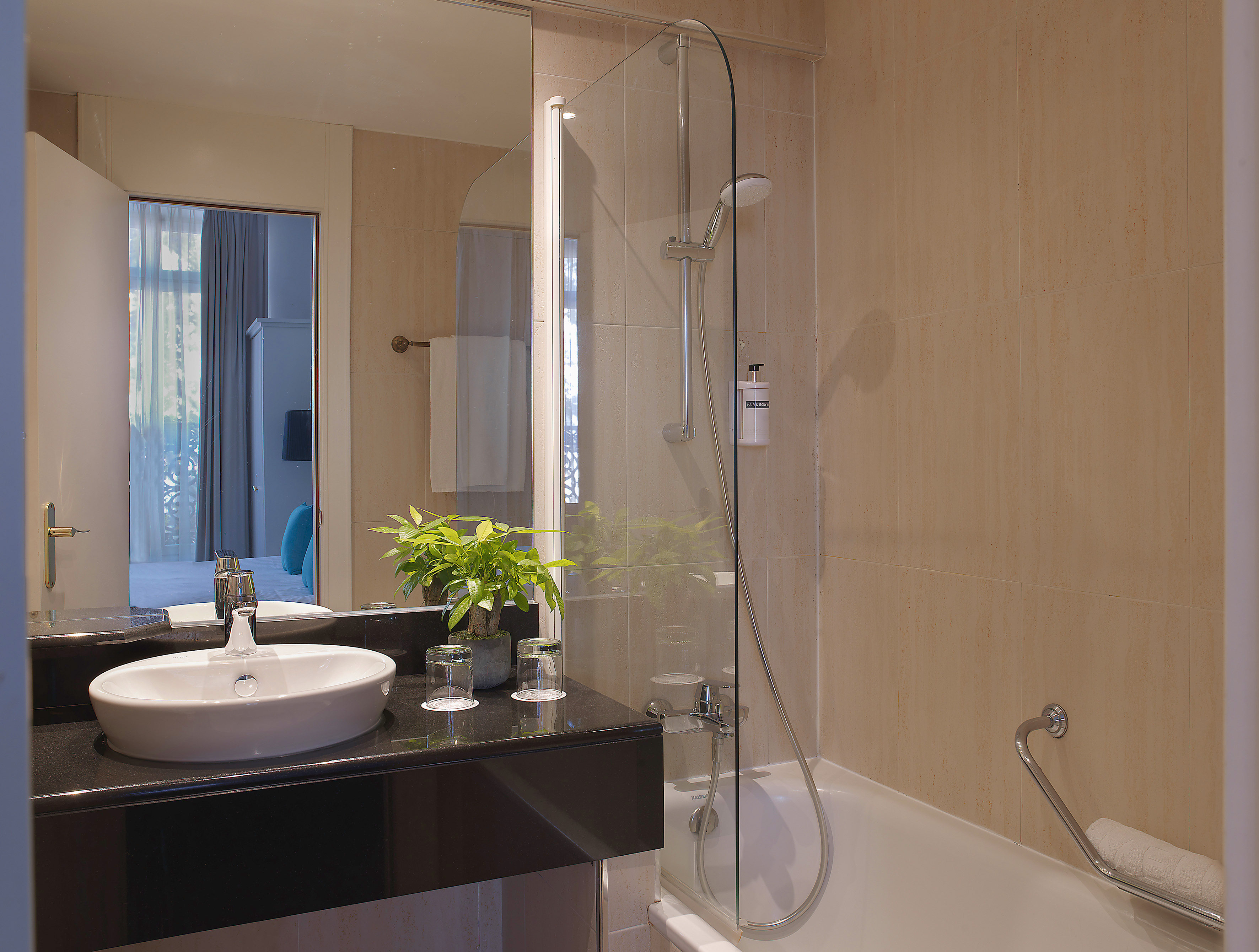 Modern hotel bathroom with sink, bathtub, glass shower, and tiled walls.