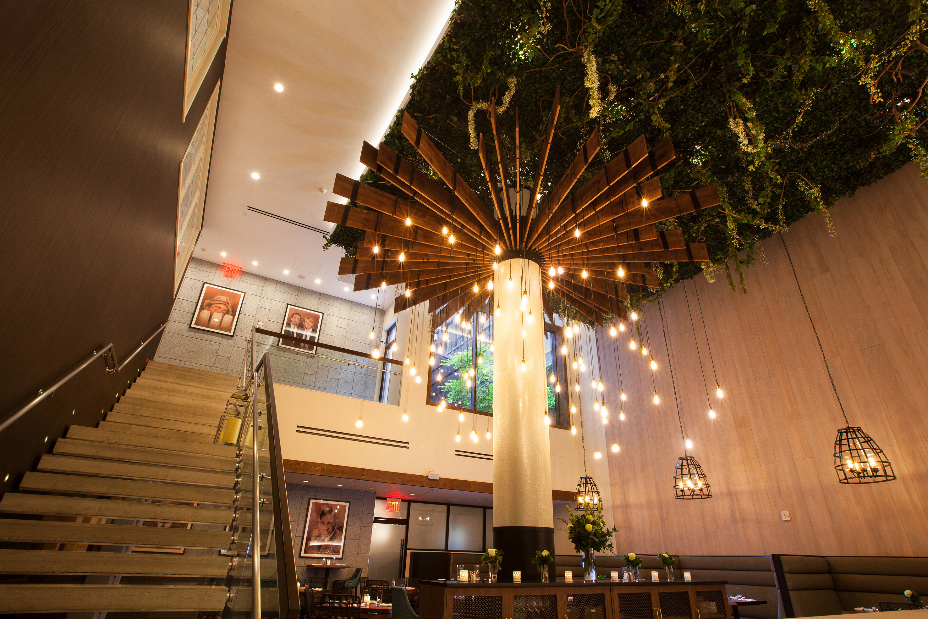 Modern restaurant interior with unique chandelier, green ceiling foliage, and staircase.