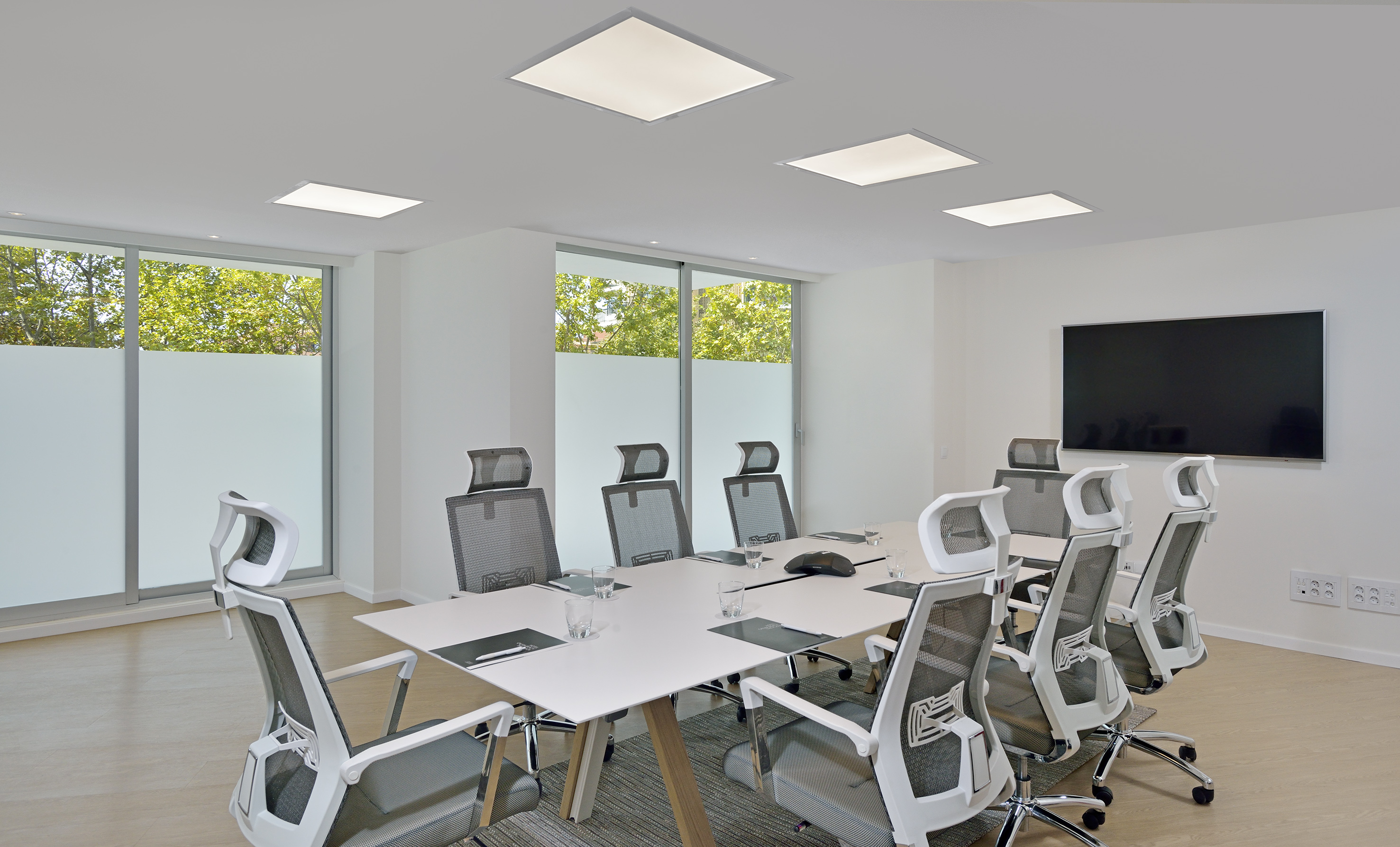 Modern meeting room with white table, ergonomic chairs, TV, and large windows.