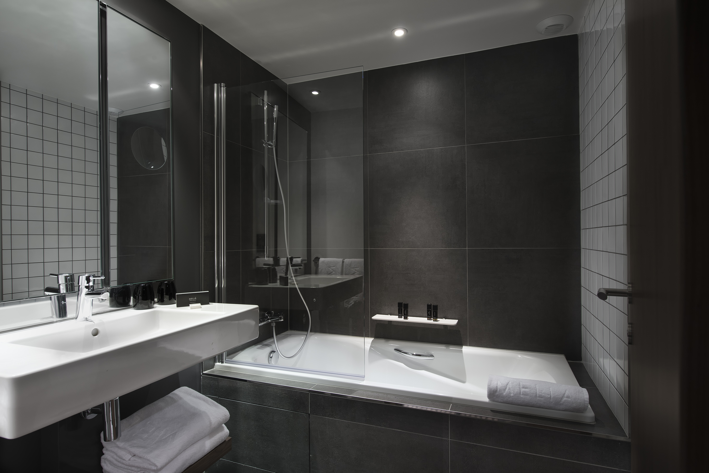 Modern hotel bathroom with dark gray tiles, white sink, bathtub, and shower.