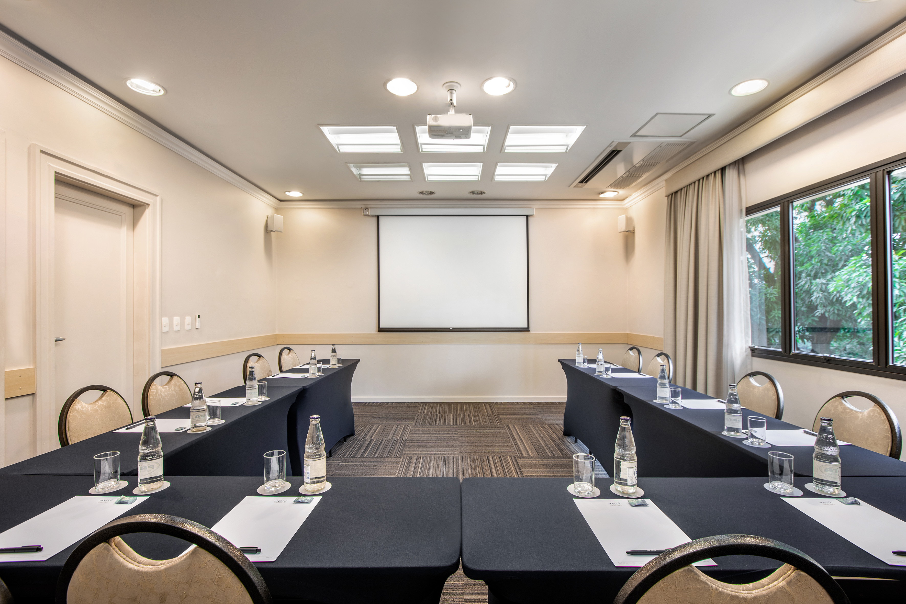 Professional conference room with U-shape table setup, projector, and window.