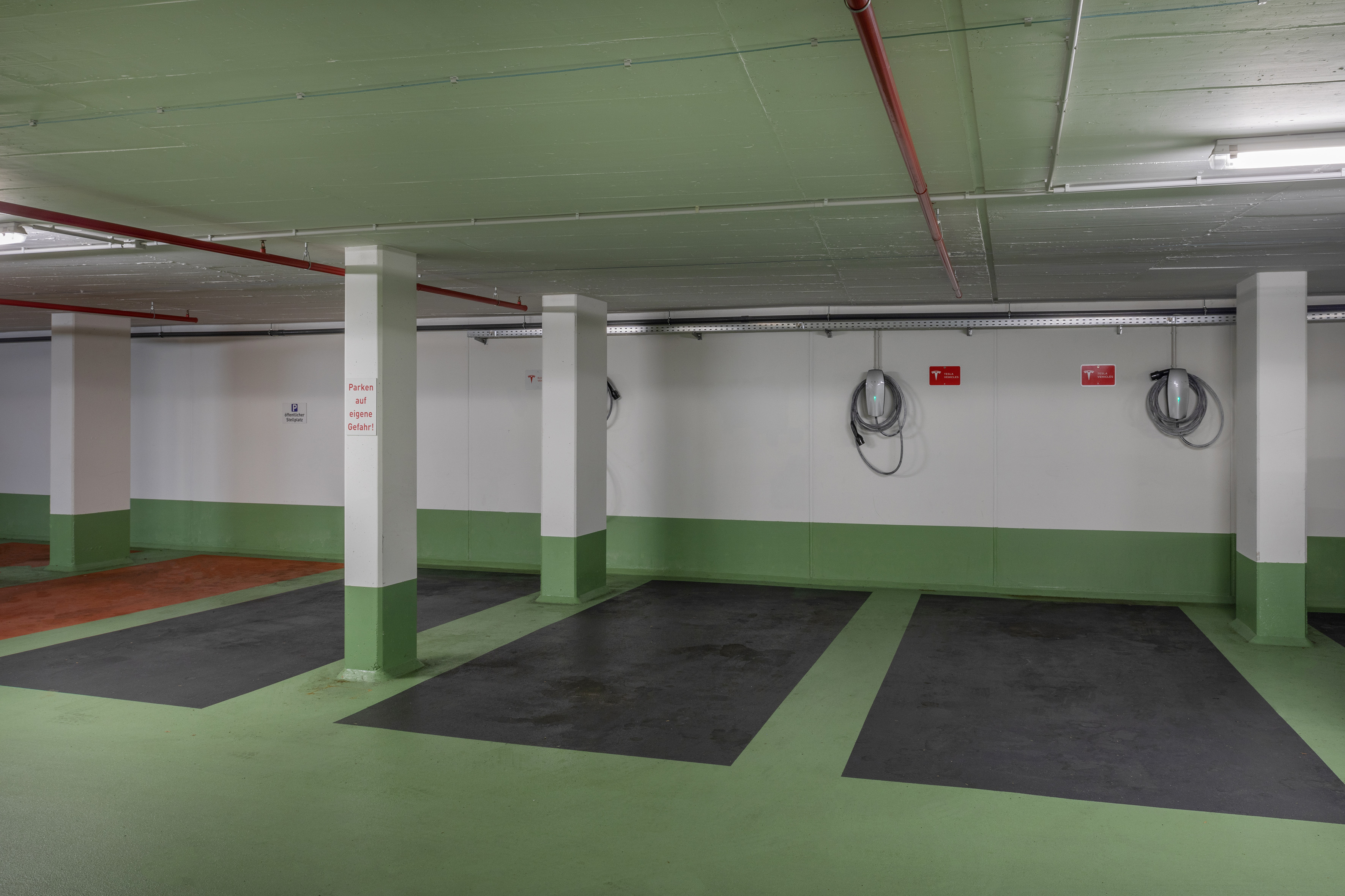 Underground parking garage with multiple Tesla EV charging stations and marked spaces.