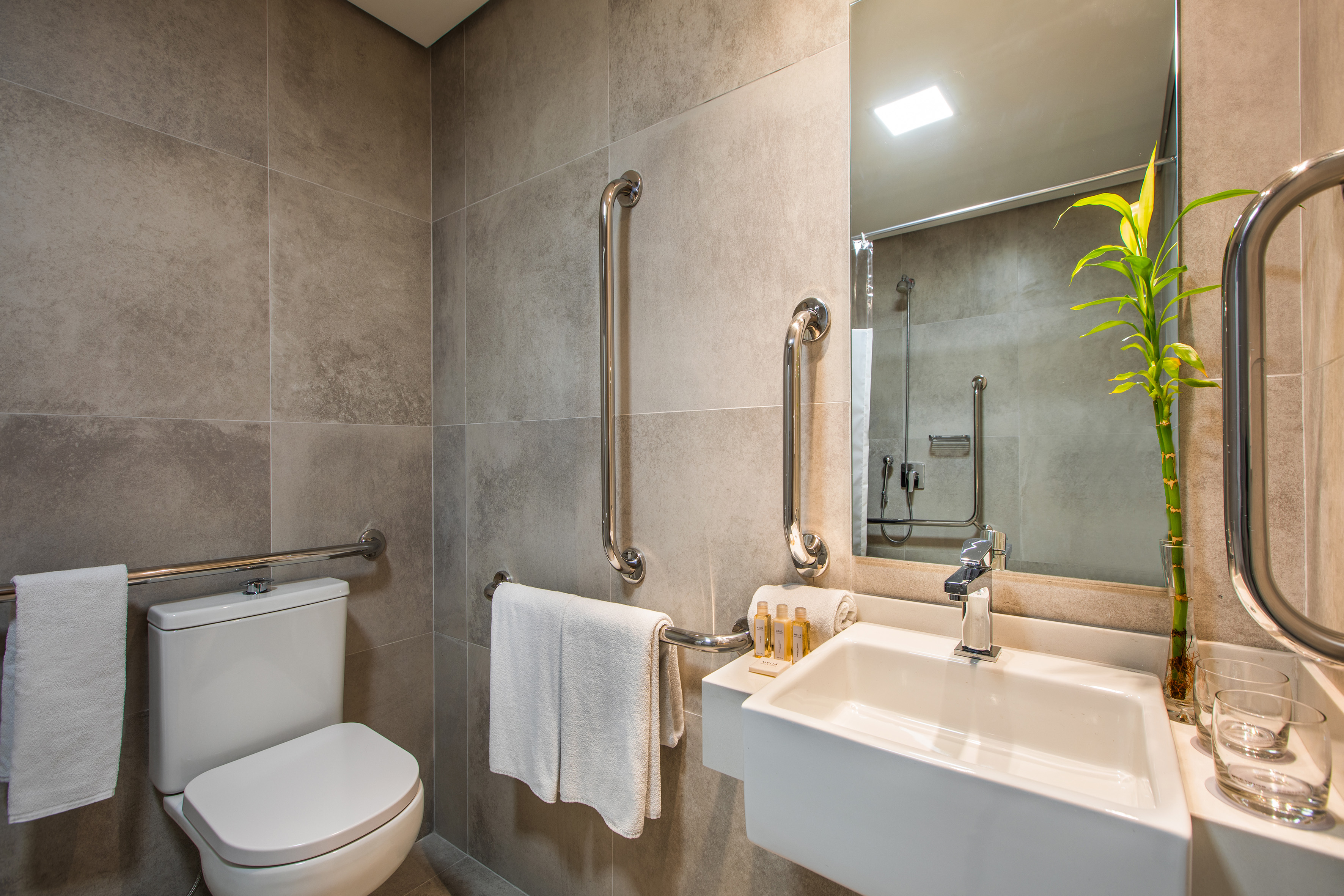 Modern ADA compliant hotel bathroom with grab bars, toilet, and sink.