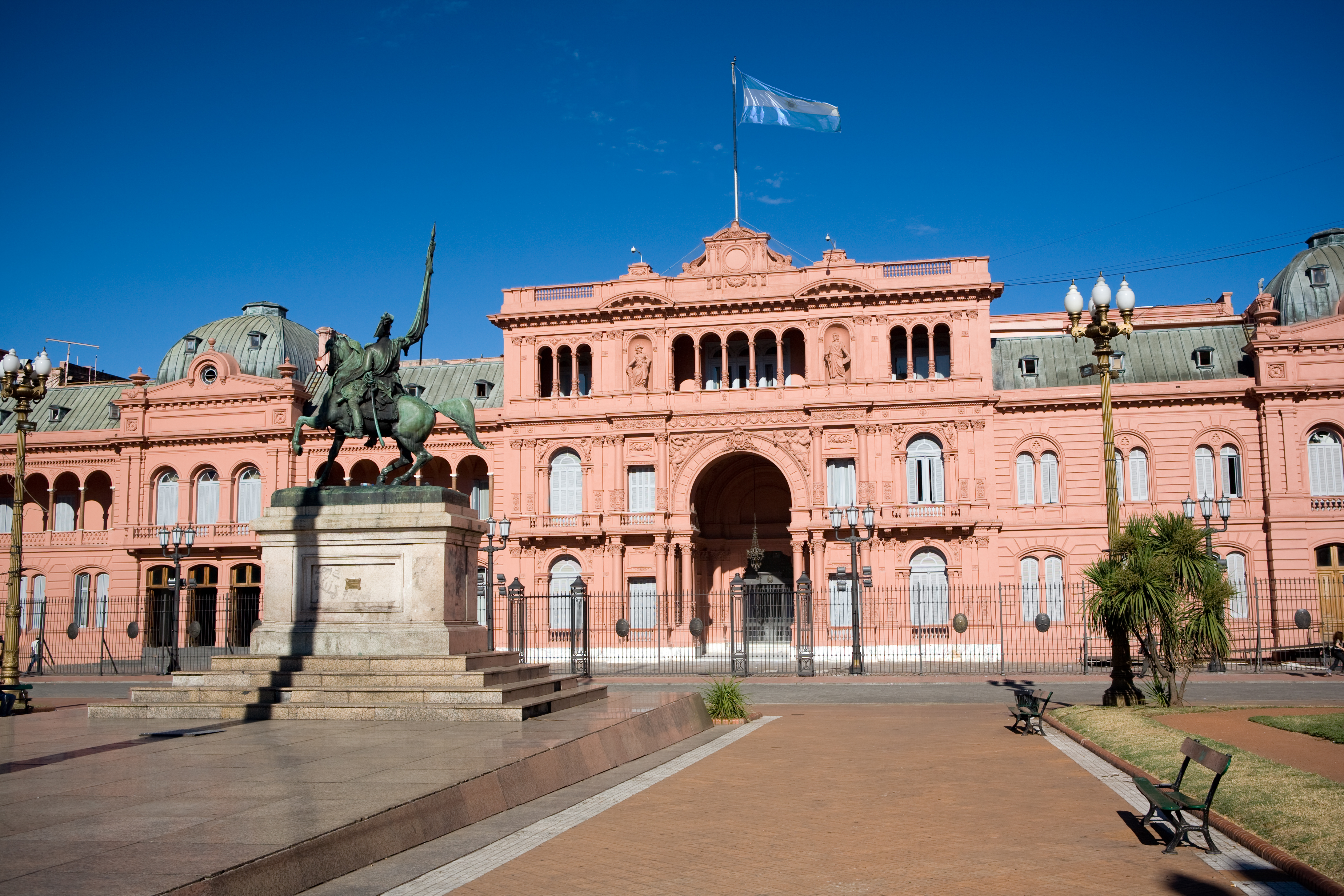 a statue of a man on a horse in front of a pink building with Casa Rosada in the background