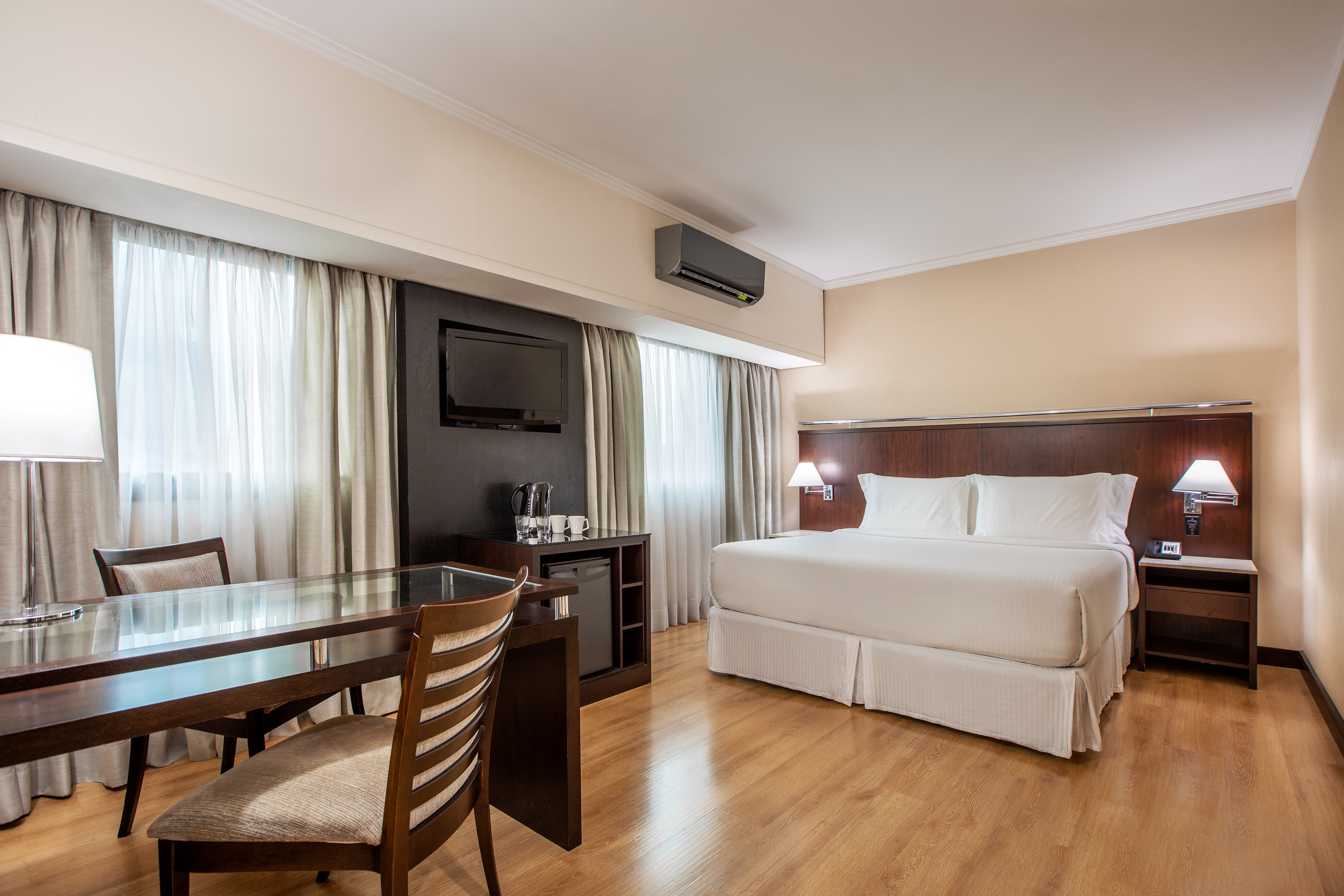 Spacious hotel room with king bed, wooden desk, TV, and hardwood floor.
