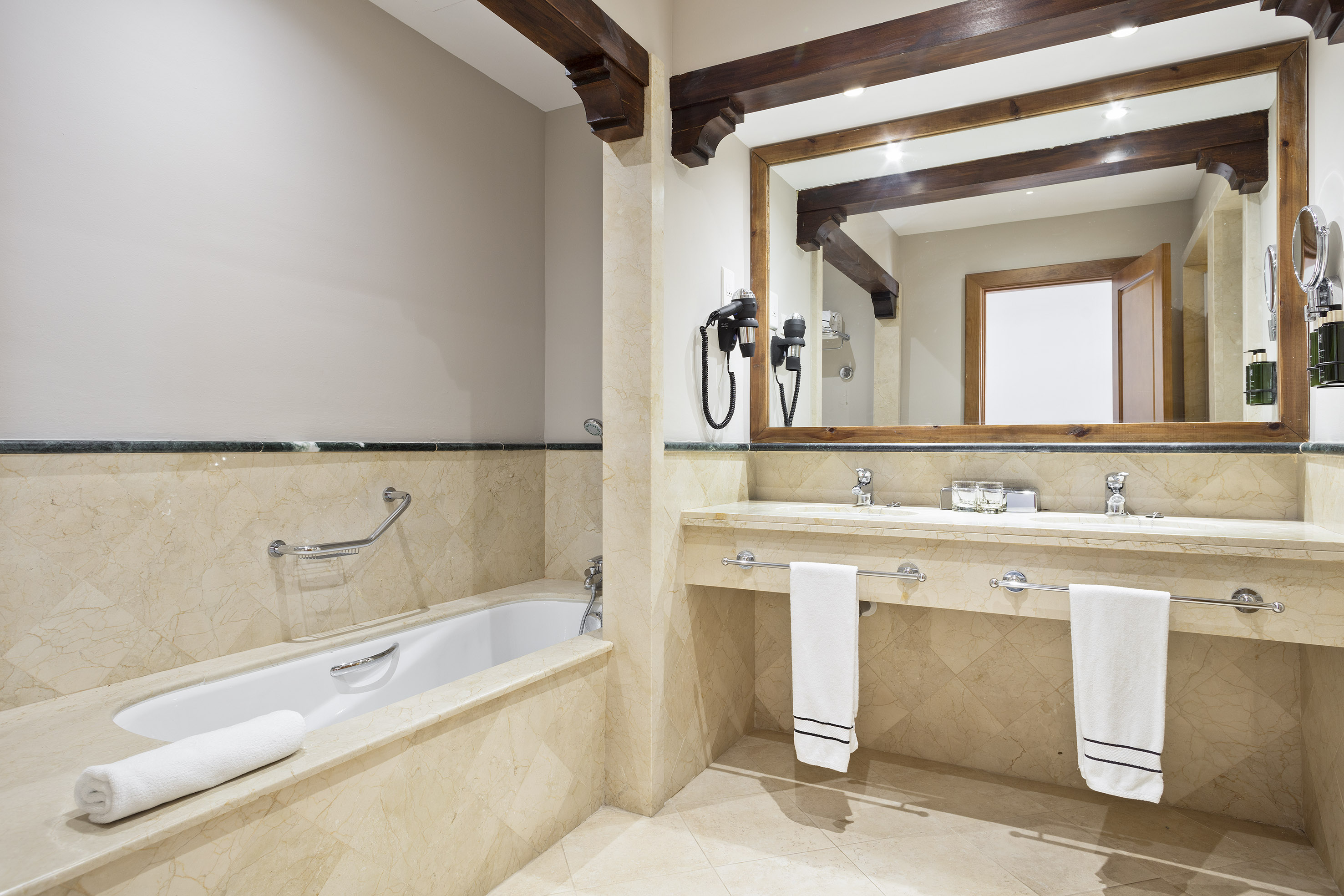 Luxury bathroom with marble bathtub, double vanity, and wooden mirror accents.