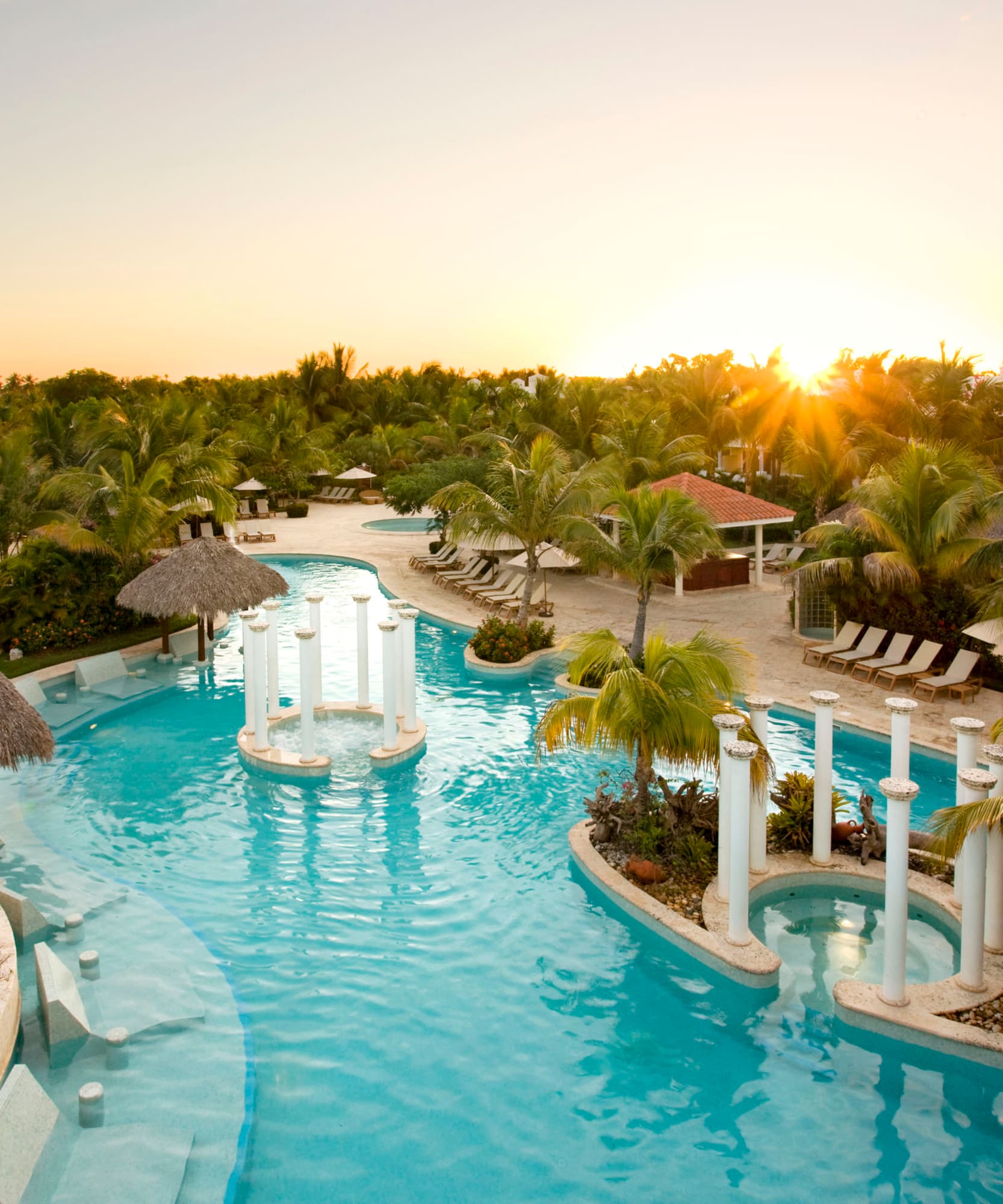 a pool with palm trees and a sun setting