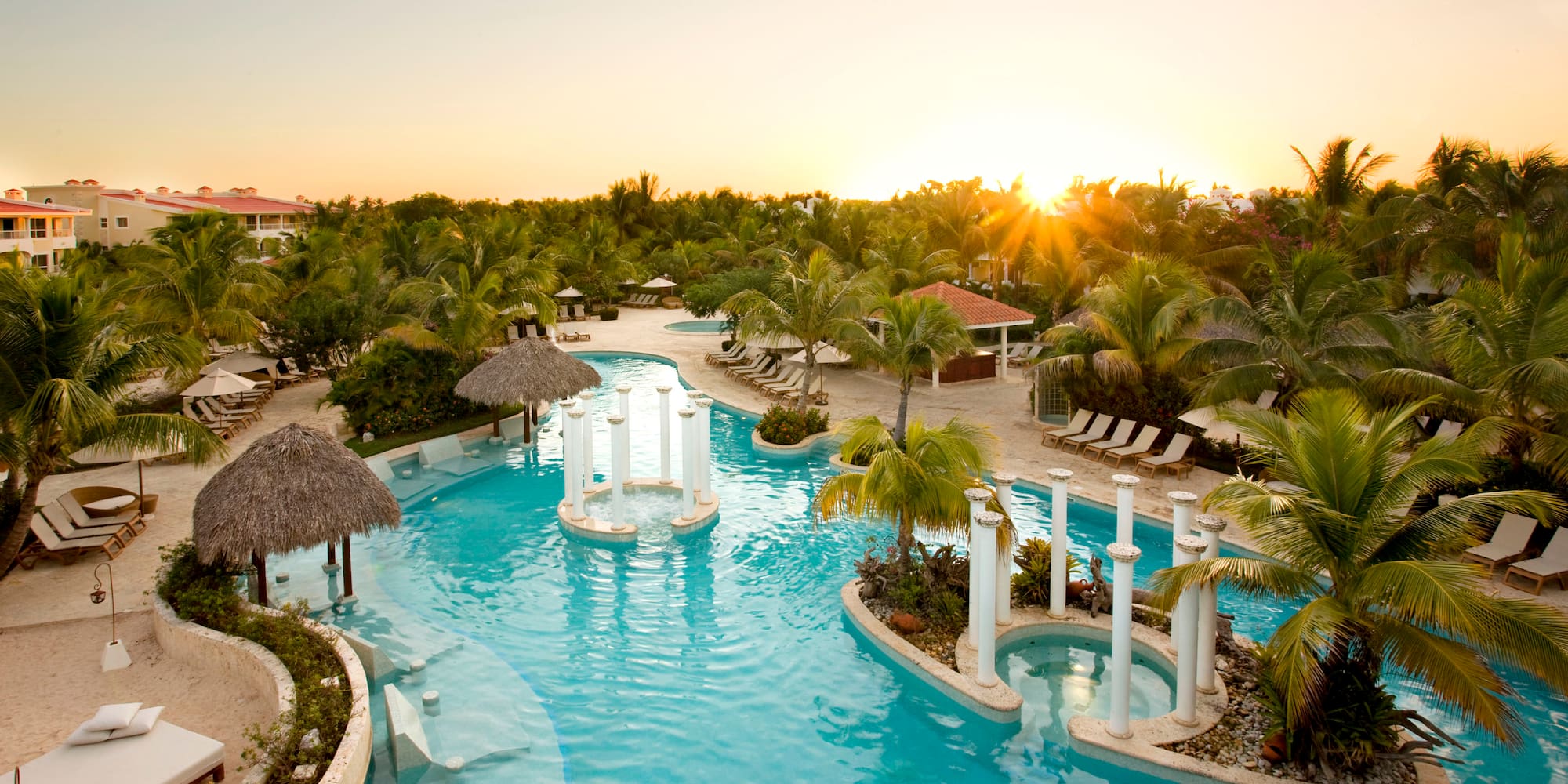 a pool with palm trees and a sun setting