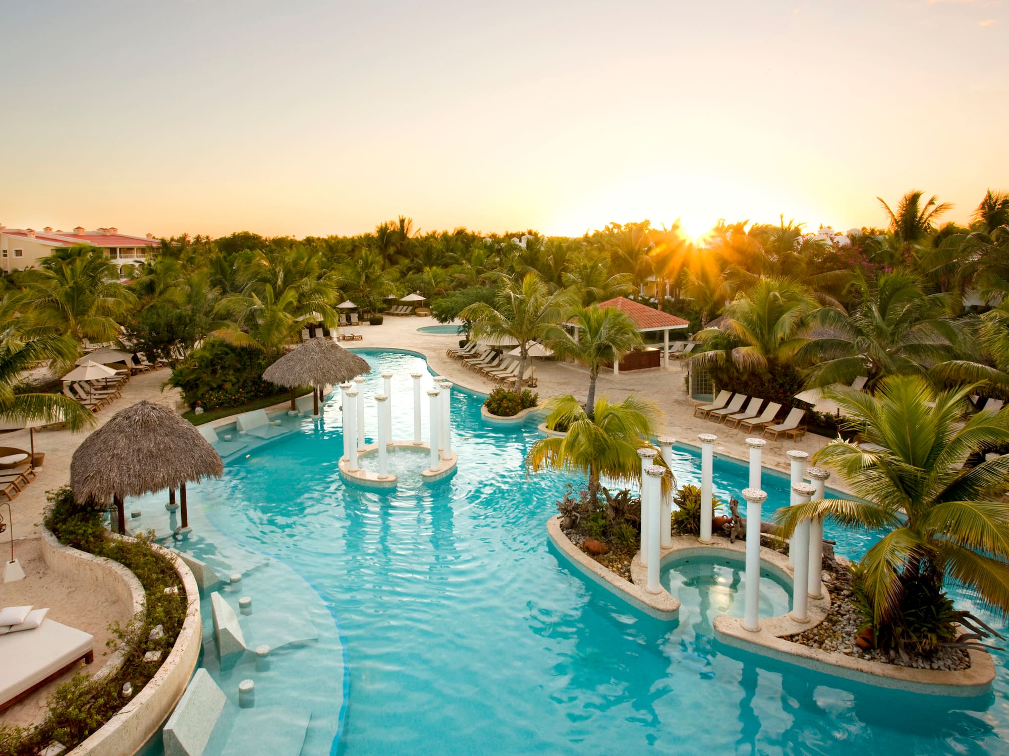 a pool with palm trees and a sun setting