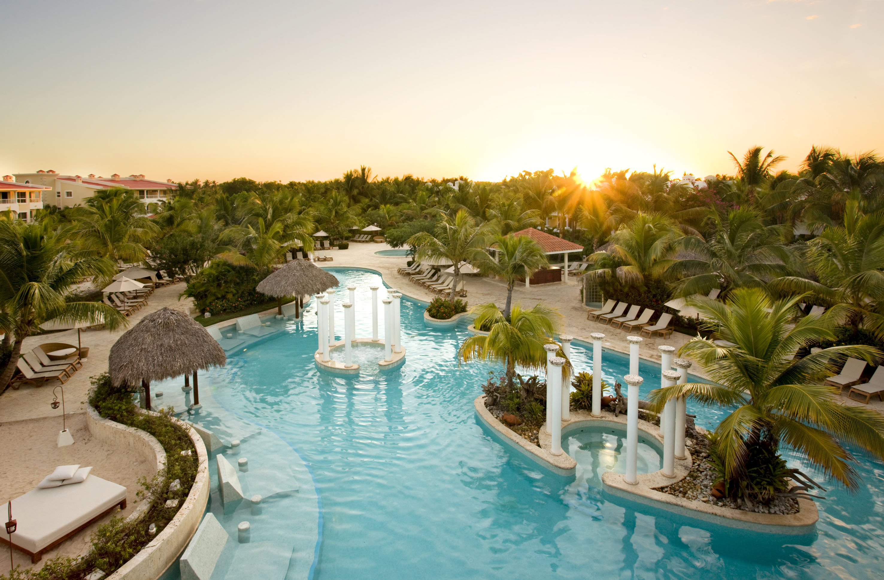 a pool with palm trees and a sun setting