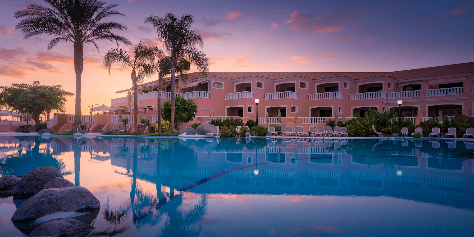 a pool with palm trees and a building with a pink sky