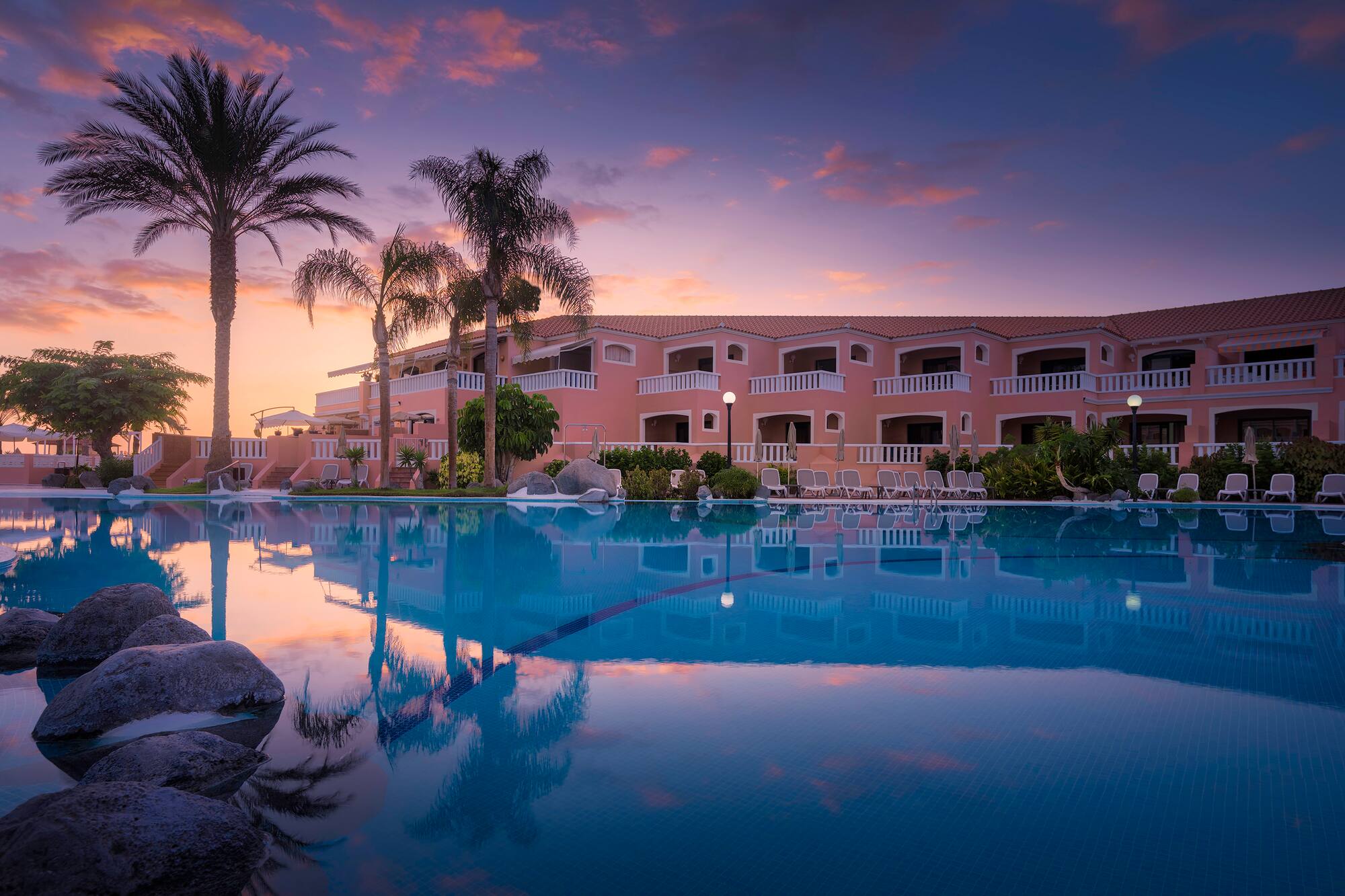 Sunset view of tropical hotel resort, pool, and palm tree reflections.