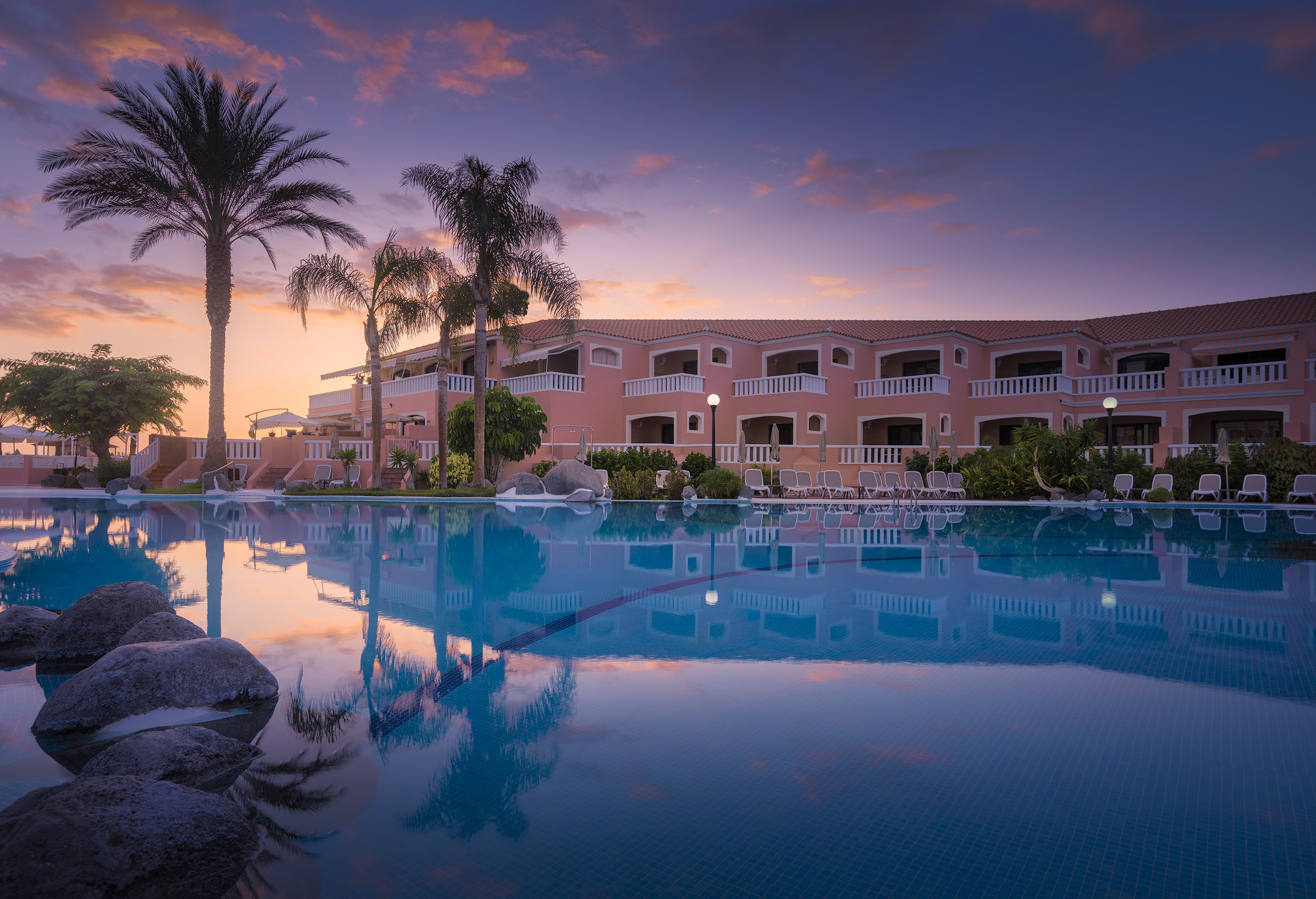 a pool with palm trees and a building with a pink sky
