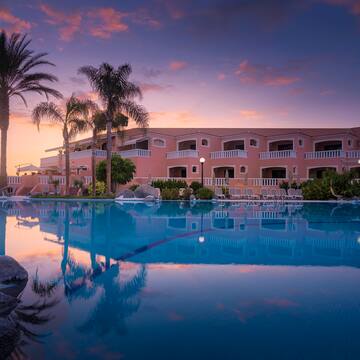 a pool with palm trees and a building with a pink sky