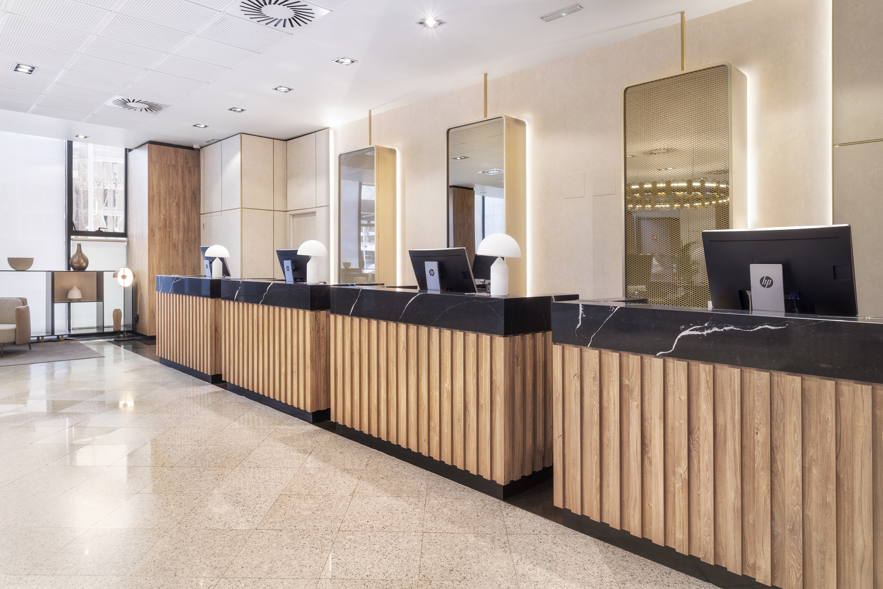 Hotel front desk with modern wood slat panels, black marble, and computers.