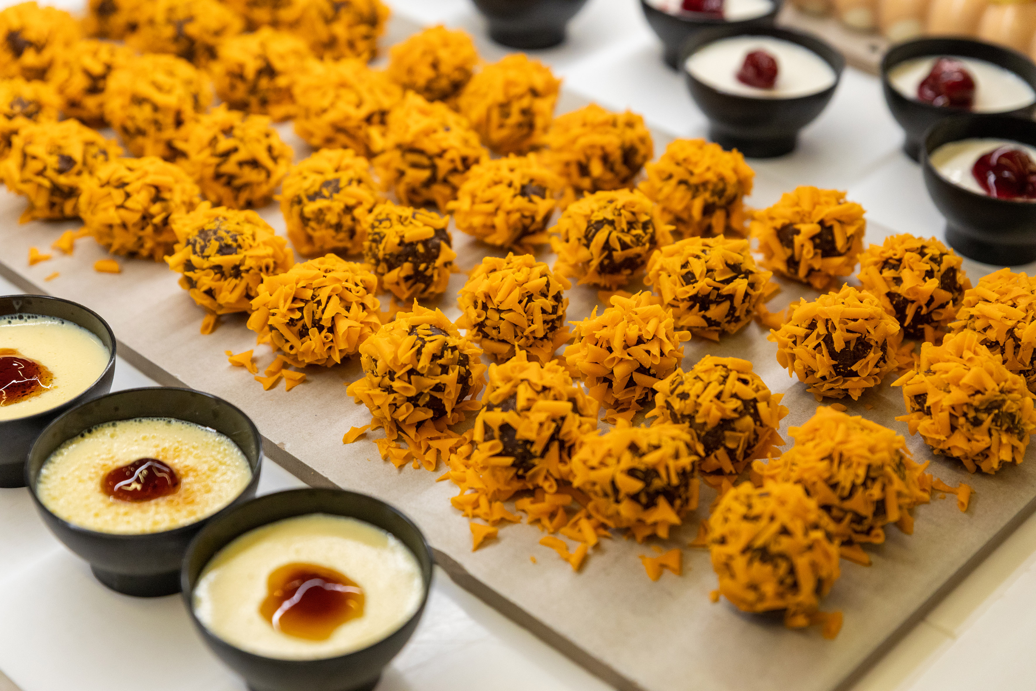 Chocolate truffles with orange flakes, creamy mini puddings on a dessert table.