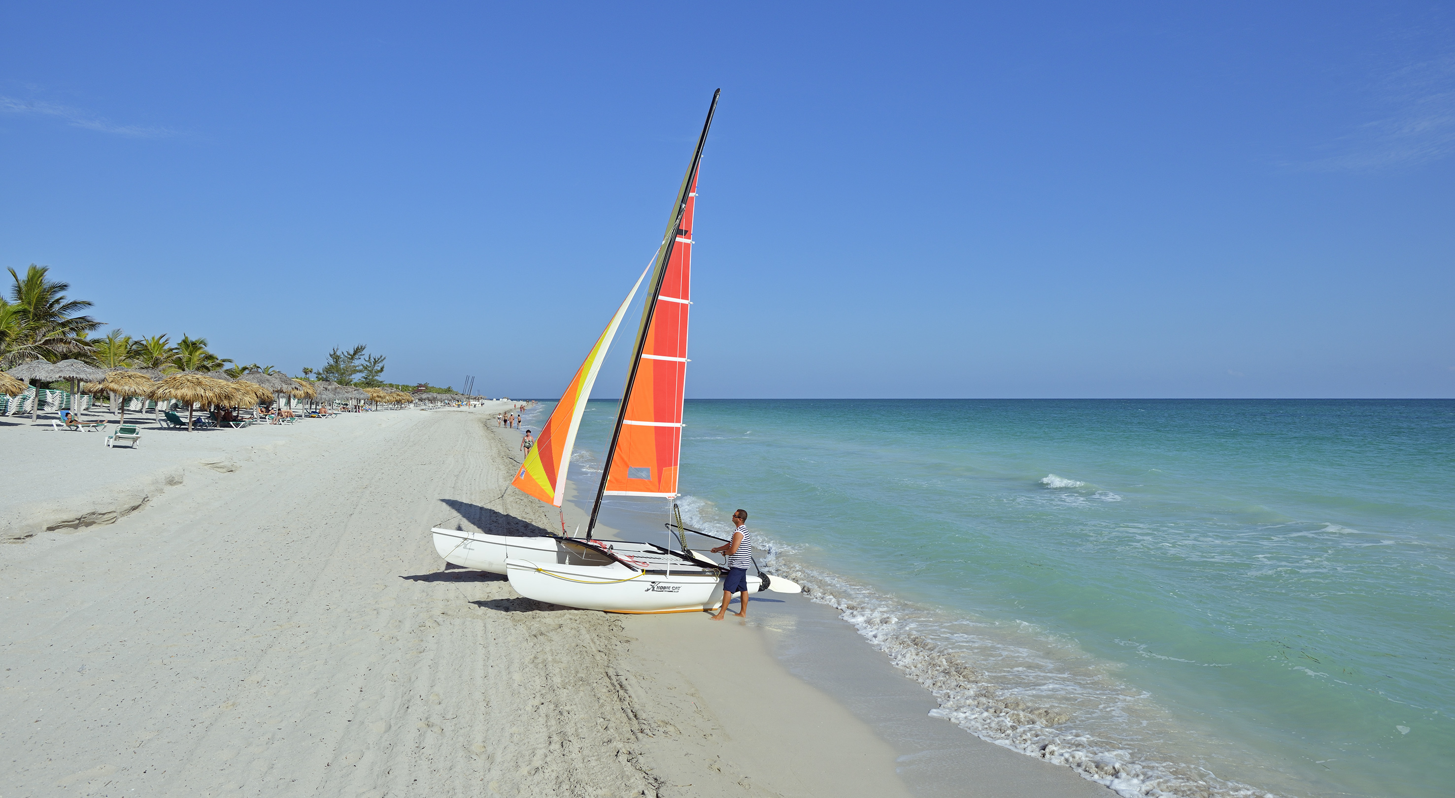 a man standing next to a sailboat on a beach