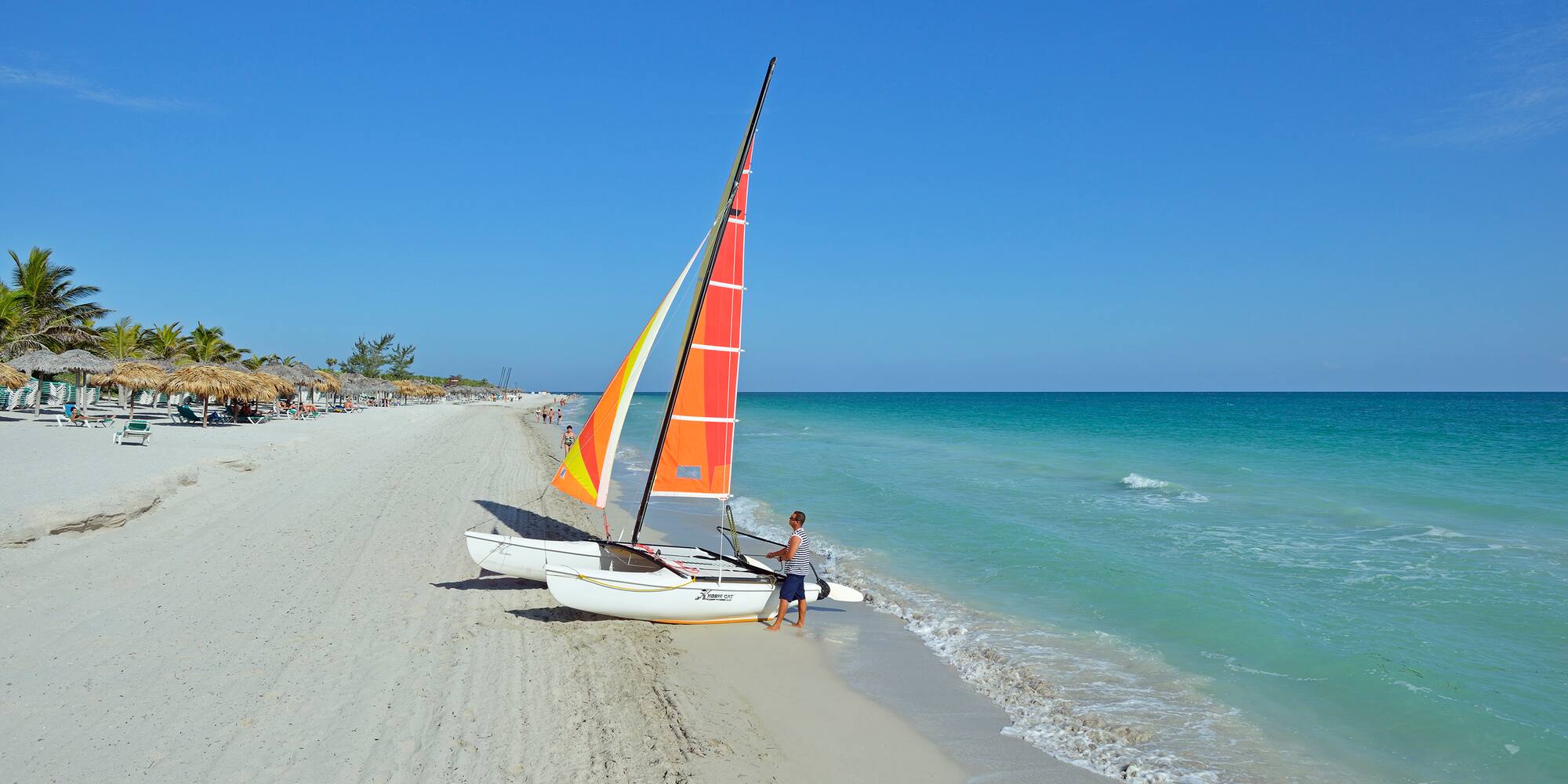a man standing next to a sailboat on a beach
