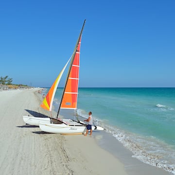 a man standing next to a sailboat on a beach