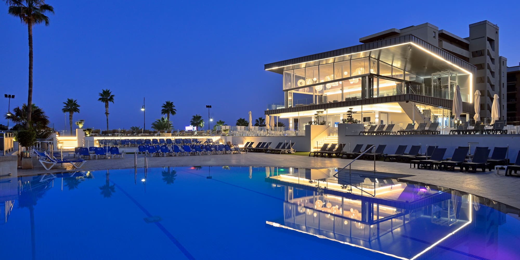 a pool with a building and a building with a pool and palm trees