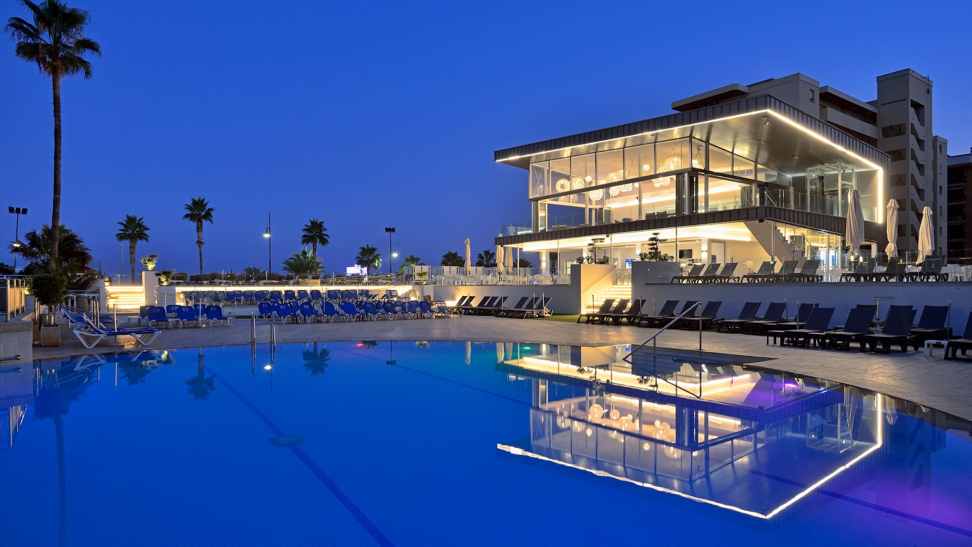 a pool with a building and a building with a pool and palm trees