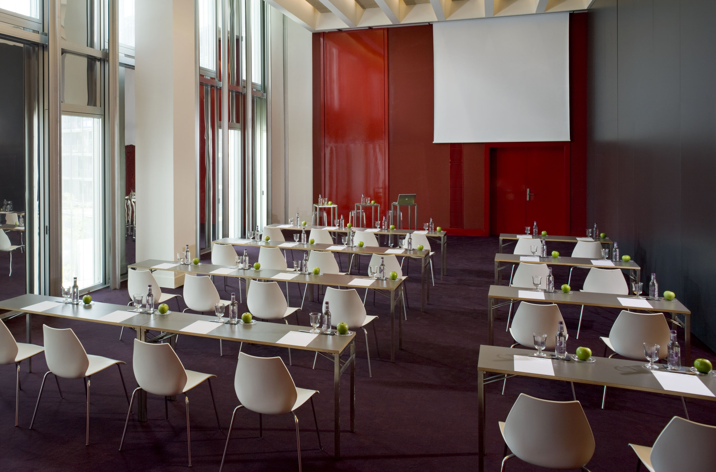 Modern conference room with rows of tables, white chairs, and projection screen.